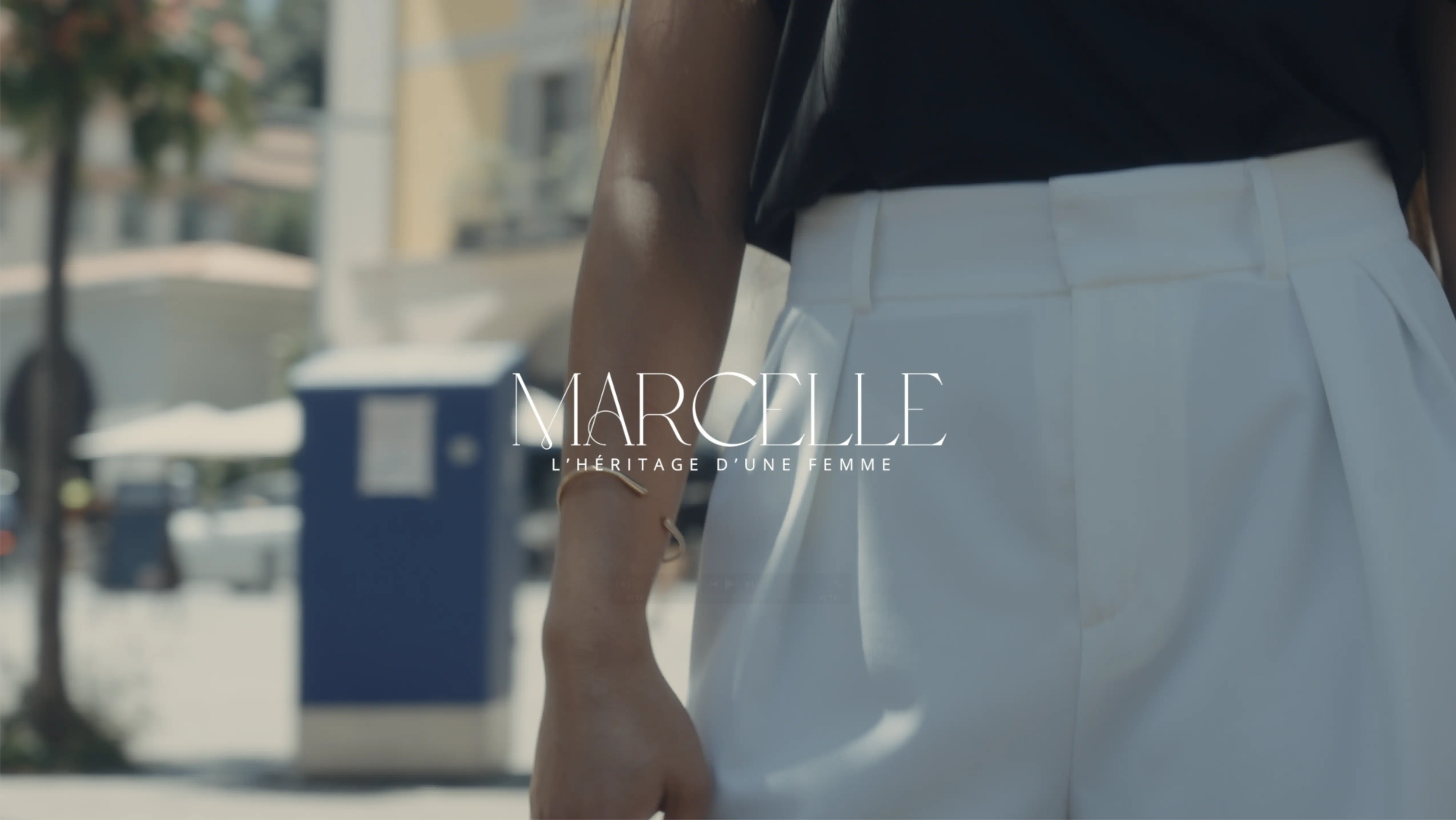 A person in stylish white high-waisted pants and a dark top is standing outdoors with a blurred city street in the background.