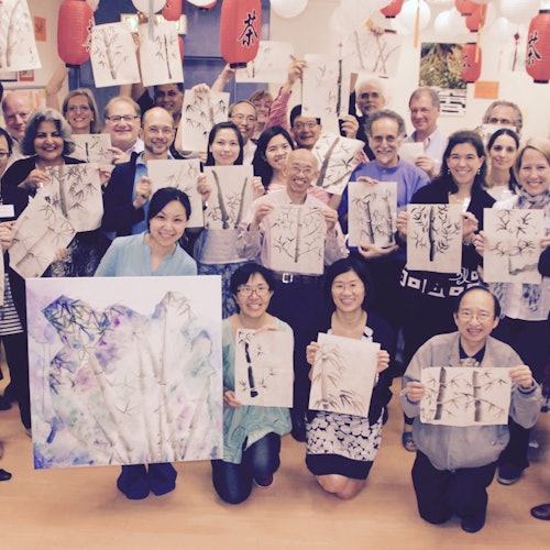 一群人自豪地在一个装饰着红灯笼、灯光明亮的房间里展示他们的画作。