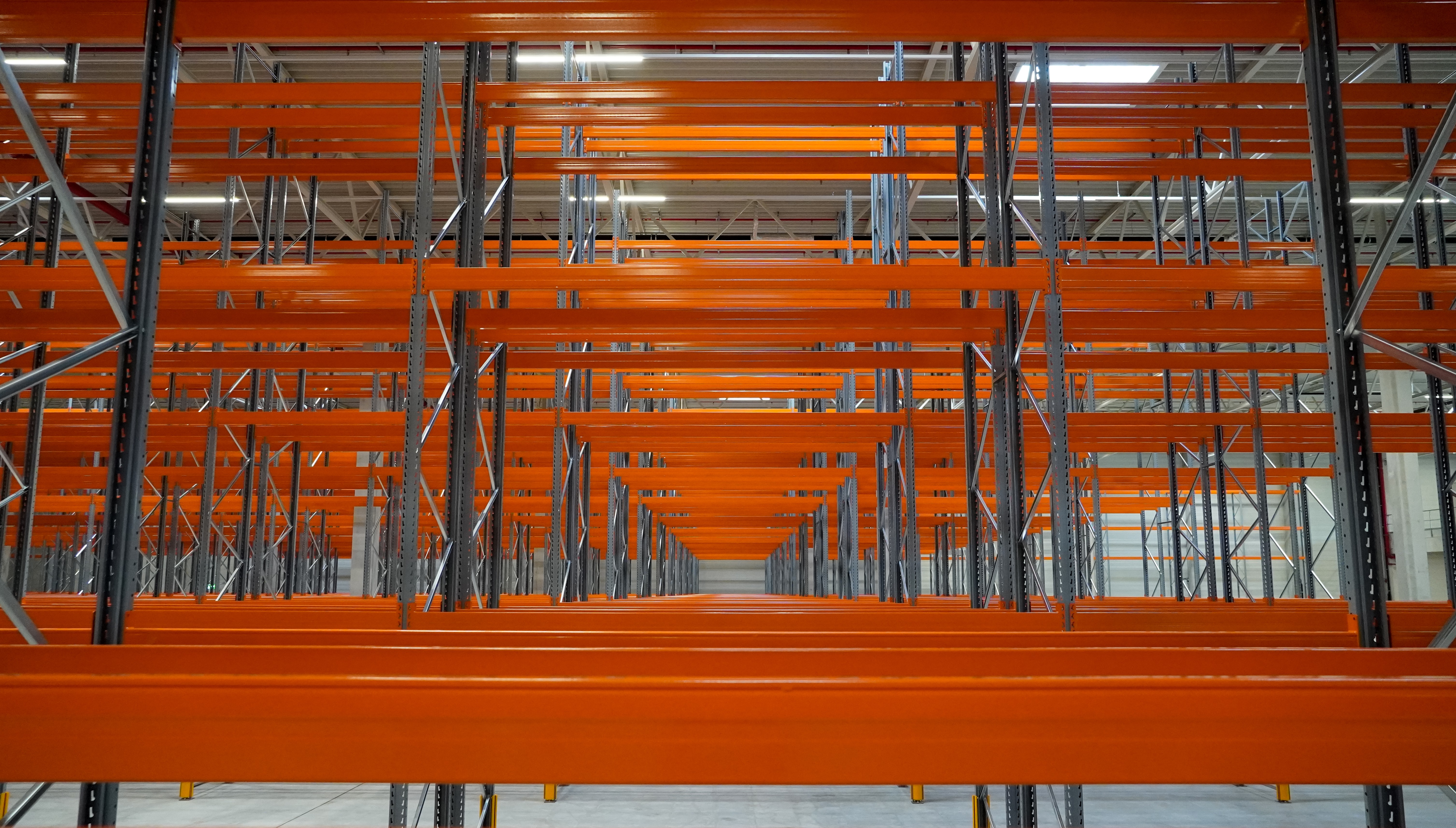 Empty industrial warehouse shelves with cantilever racking, featuring repetitive rows of orange beams and metallic frames, convey an organized yet vacant atmosphere.
