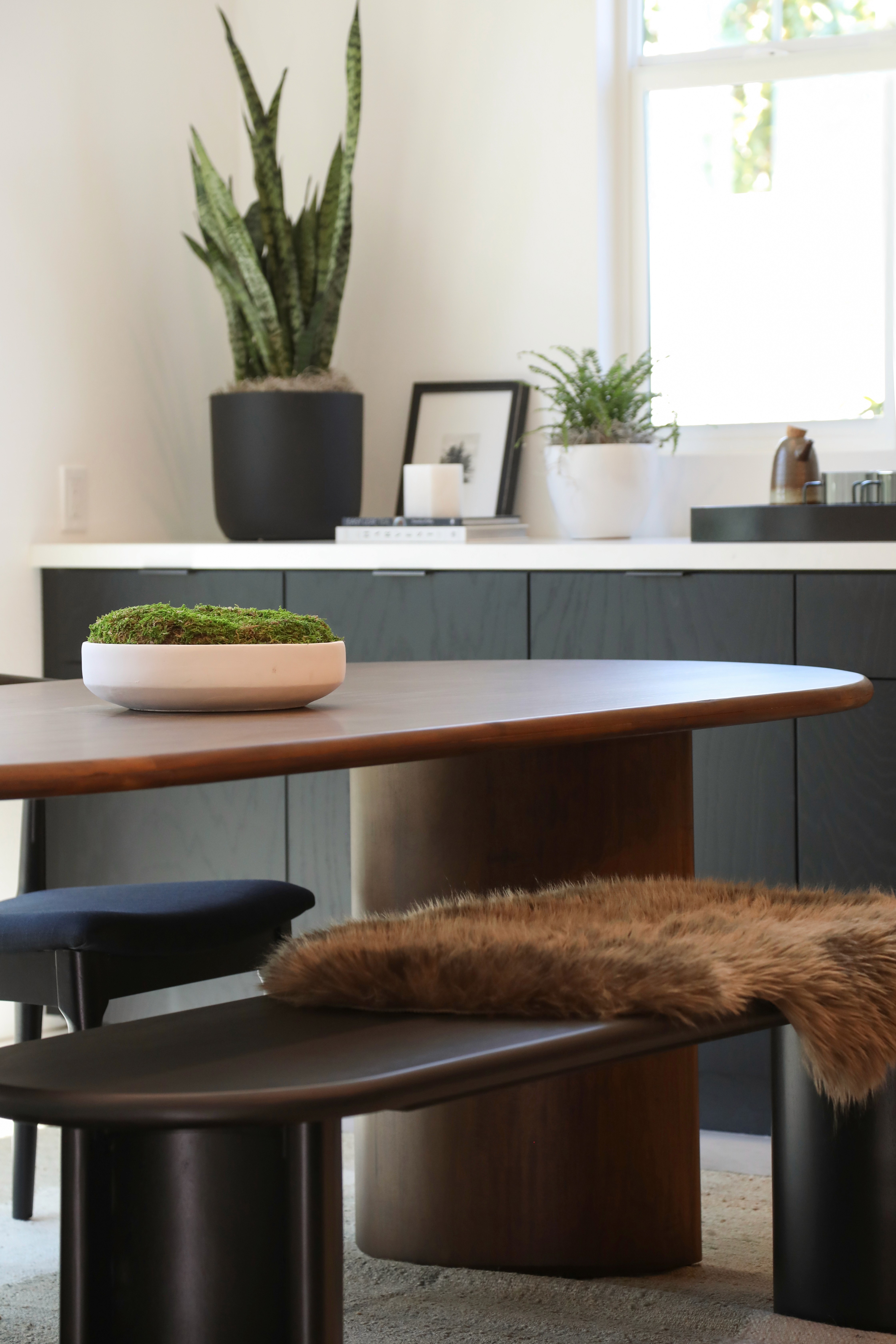 Dining area with rounded wooden table and bench seating, black cabinetry with white countertops by Jubilee Interiors in Arcadia, California