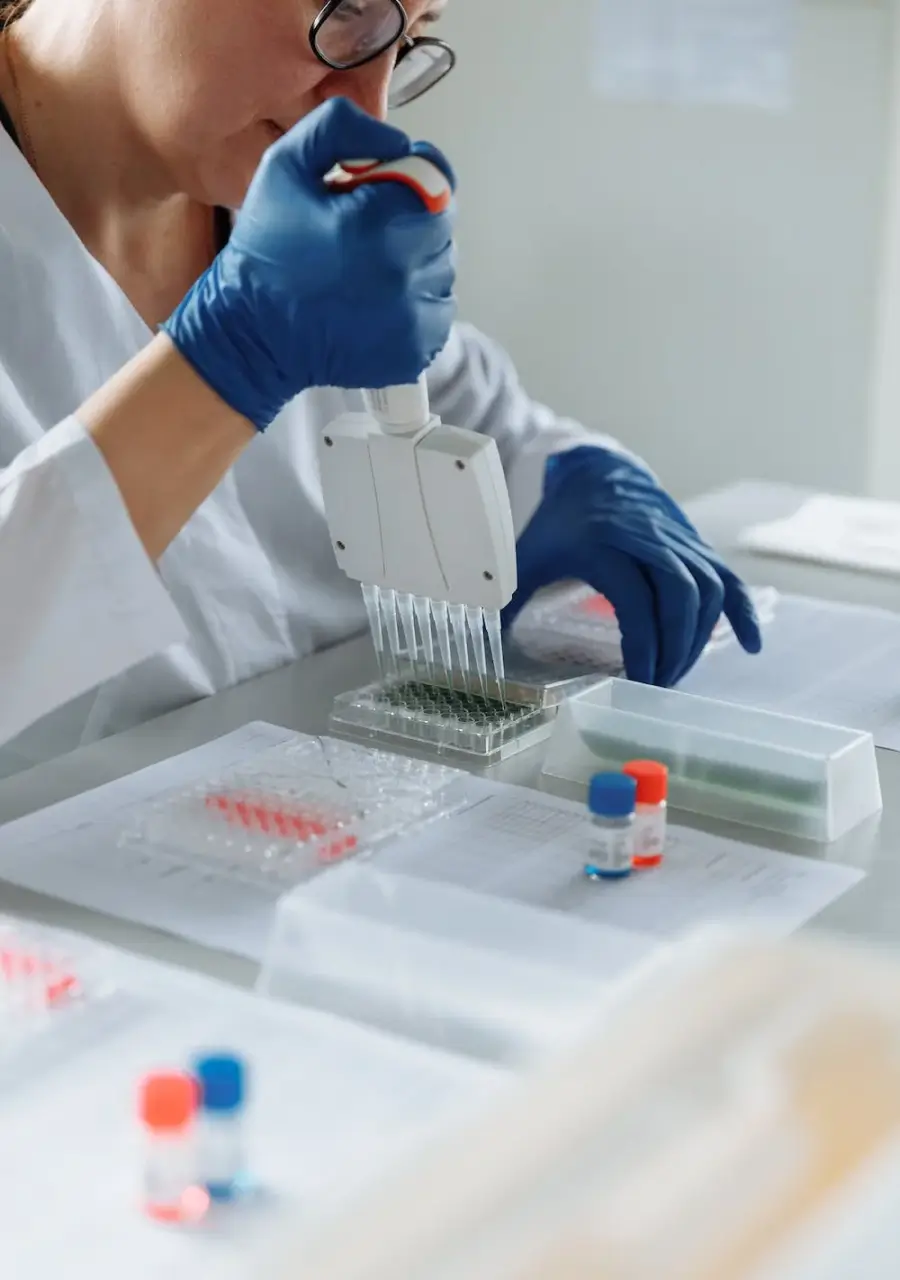 Scientist using a multi-channel pipette to transfer liquid samples in a lab, wearing gloves and surrounded by lab equipment.