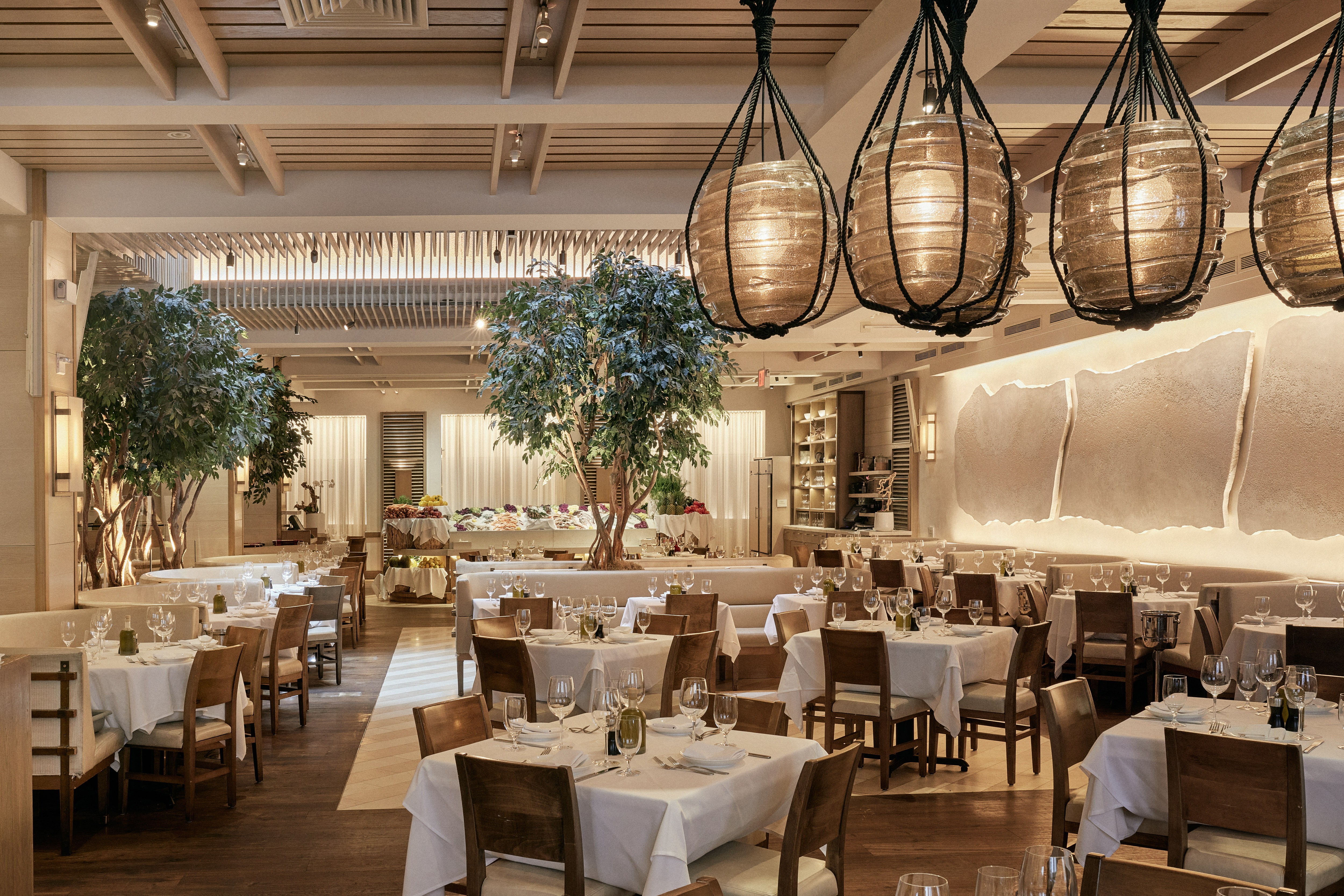 A stylish restaurant interior featuring wooden tables, bright lighting, and lush greenery decor.
