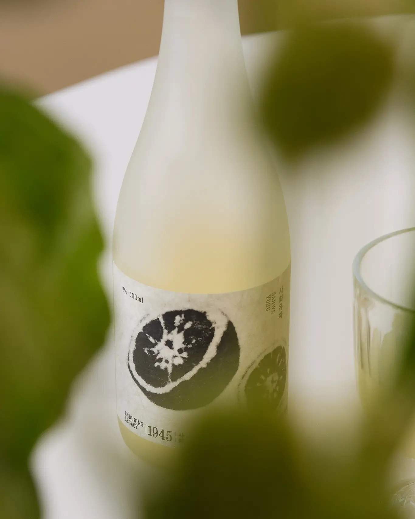 A frosted glass bottle of Sahwa Yuzu, a Korean fruit wine, is visible through out-of-focus foliage