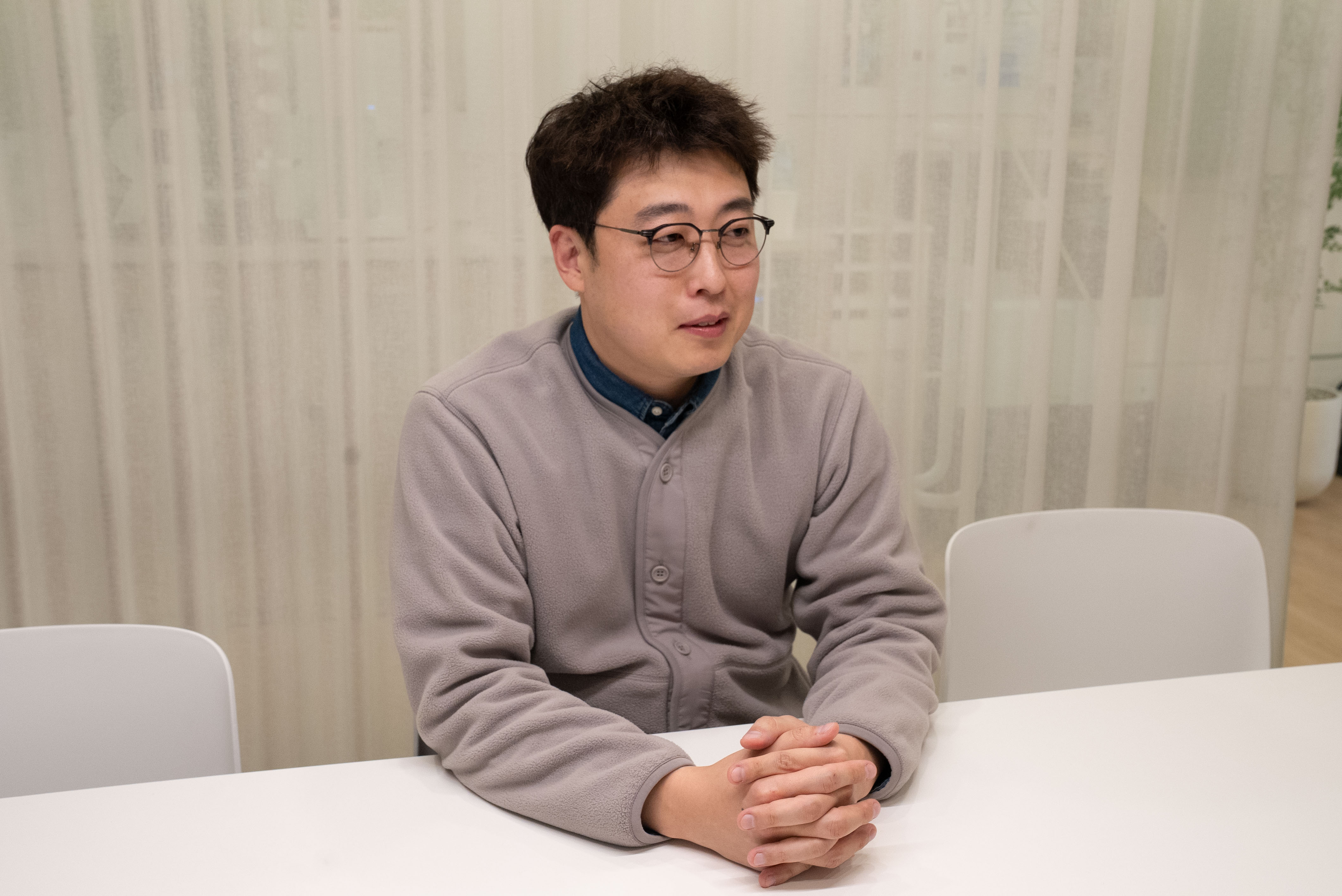 흰색 테이블에 두 손을 모으고 앉아 인터뷰에 응하고 있는 포스트엠비 어지환 과장의 모습입니다.