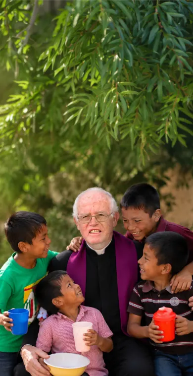 El Padre Luis Miró Quesada sonriendo junto a un grupo de niños, representando la labor social de la campaña de donaciones de Traperos de Emaús Samaritano.