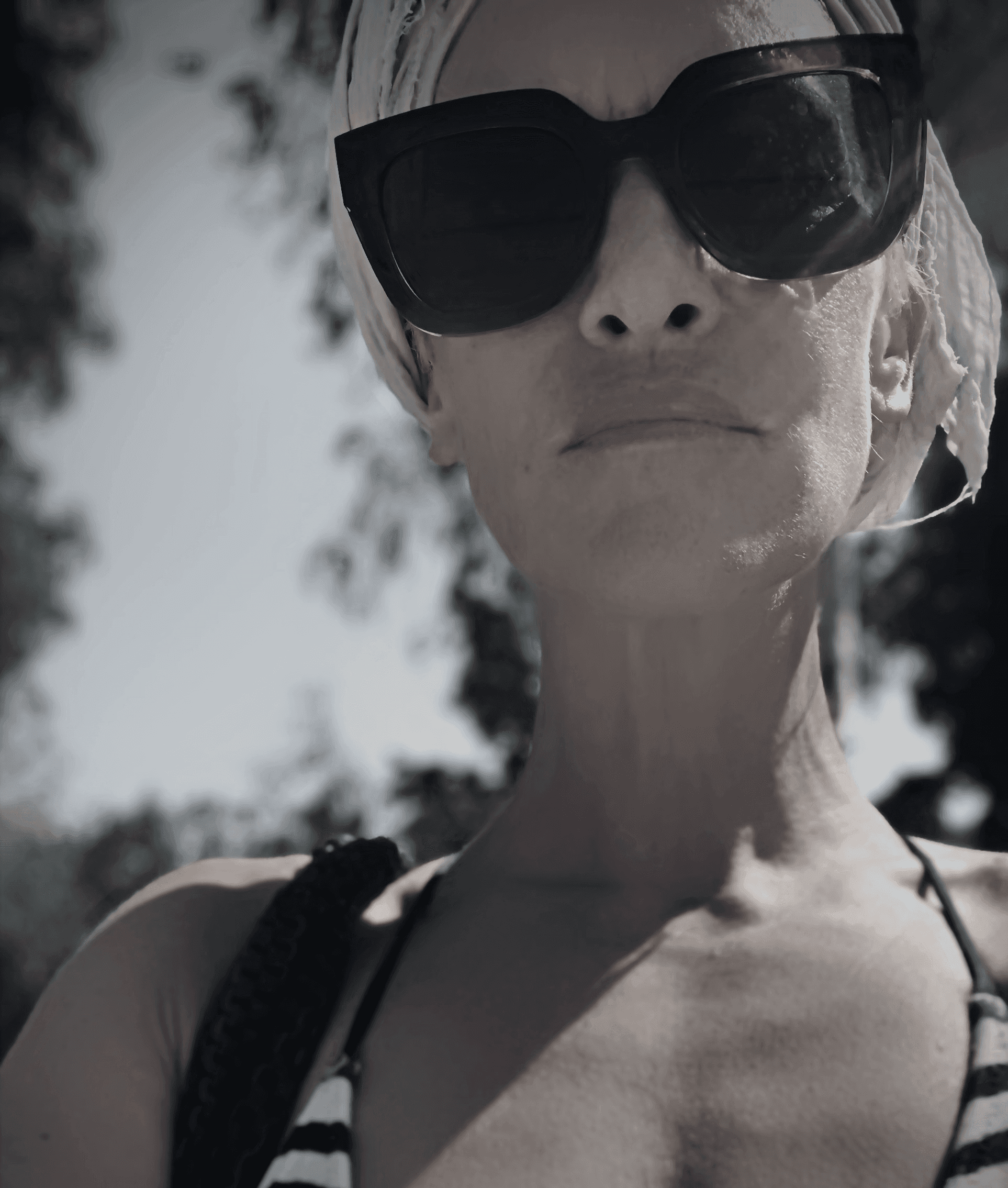 Una persona con una camiseta negra y pantalones de color claro está de pie en la cima rocosa de una montaña al atardecer, sosteniendo una cámara frente a su cara para tomar una foto. Un mar de nubes se extiende detrás de ellos, iluminado por la luz dorada del sol poniente.