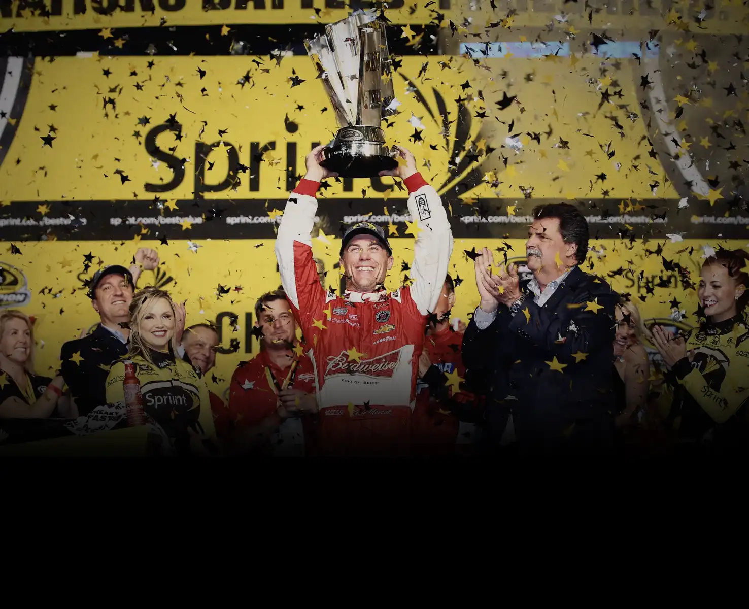 Kevin Harvick hoisting a trophy over his head with confetti falling all around him. 