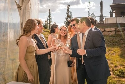 Wedding guests smile and raise champagne glasses together beside the cabin.