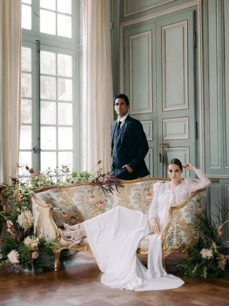 Fashion-forward wedding couple posing in a classic European-style room, showcasing the opulent and dramatic appeal of editorial wedding photography.