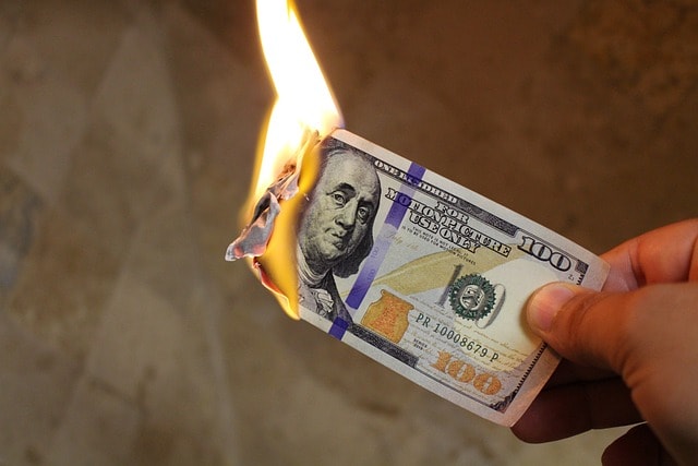 Hand holding a burning $100 bill