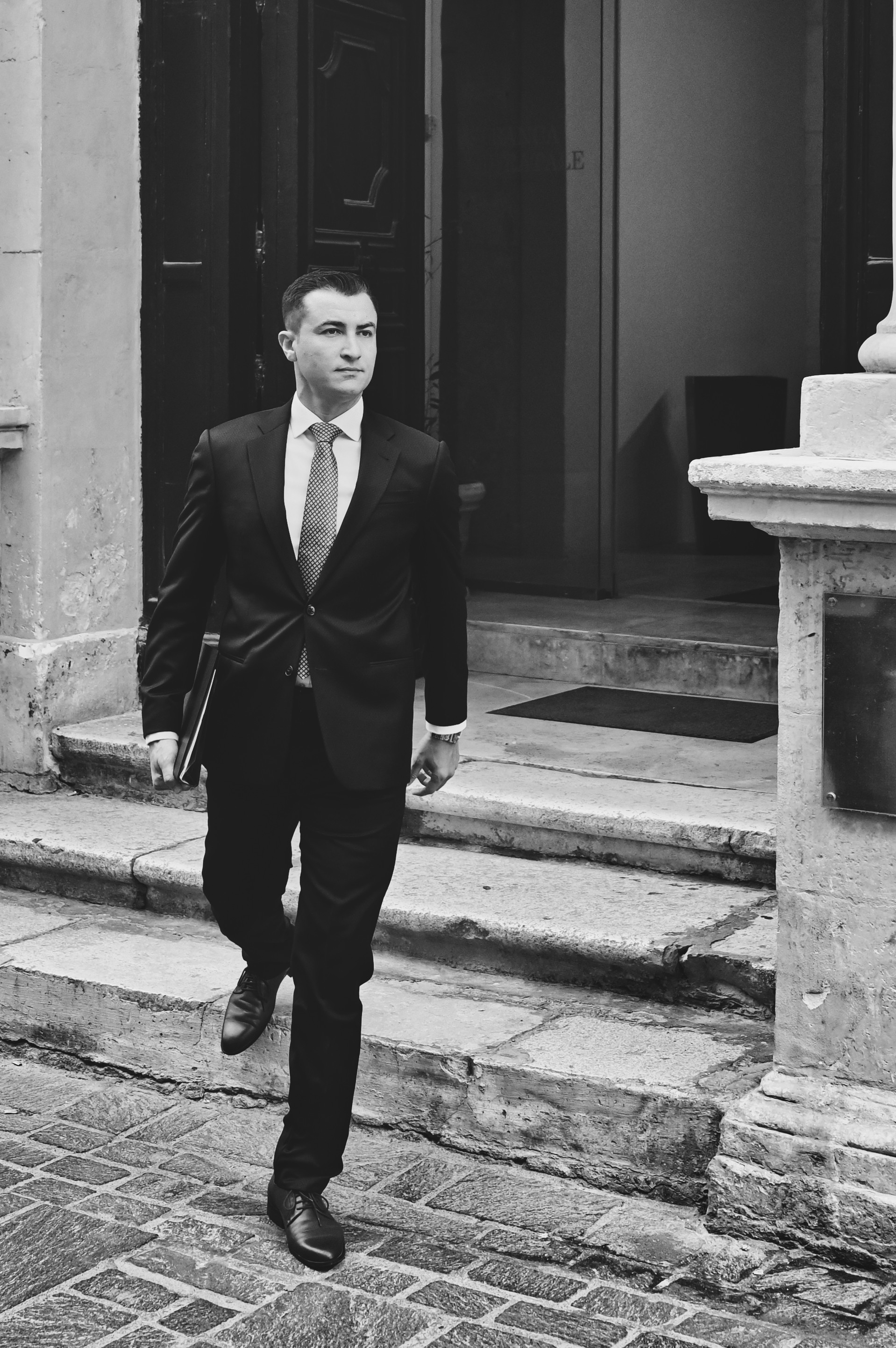 Man in a dark suit walking down stone steps, black and white
