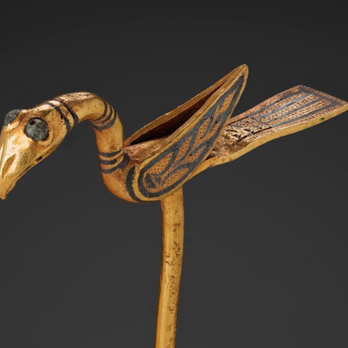 Wooden bird sculpture with decorative patterns and large eyes, viewed against a dark gray background.
