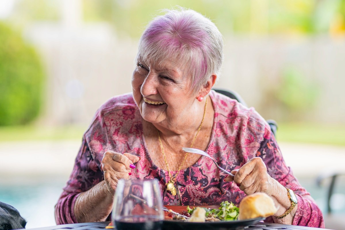 A smiling older woman enjoying a fresh salad at an outdoor table, capturing the pleasure of eating well and aging with confidence.