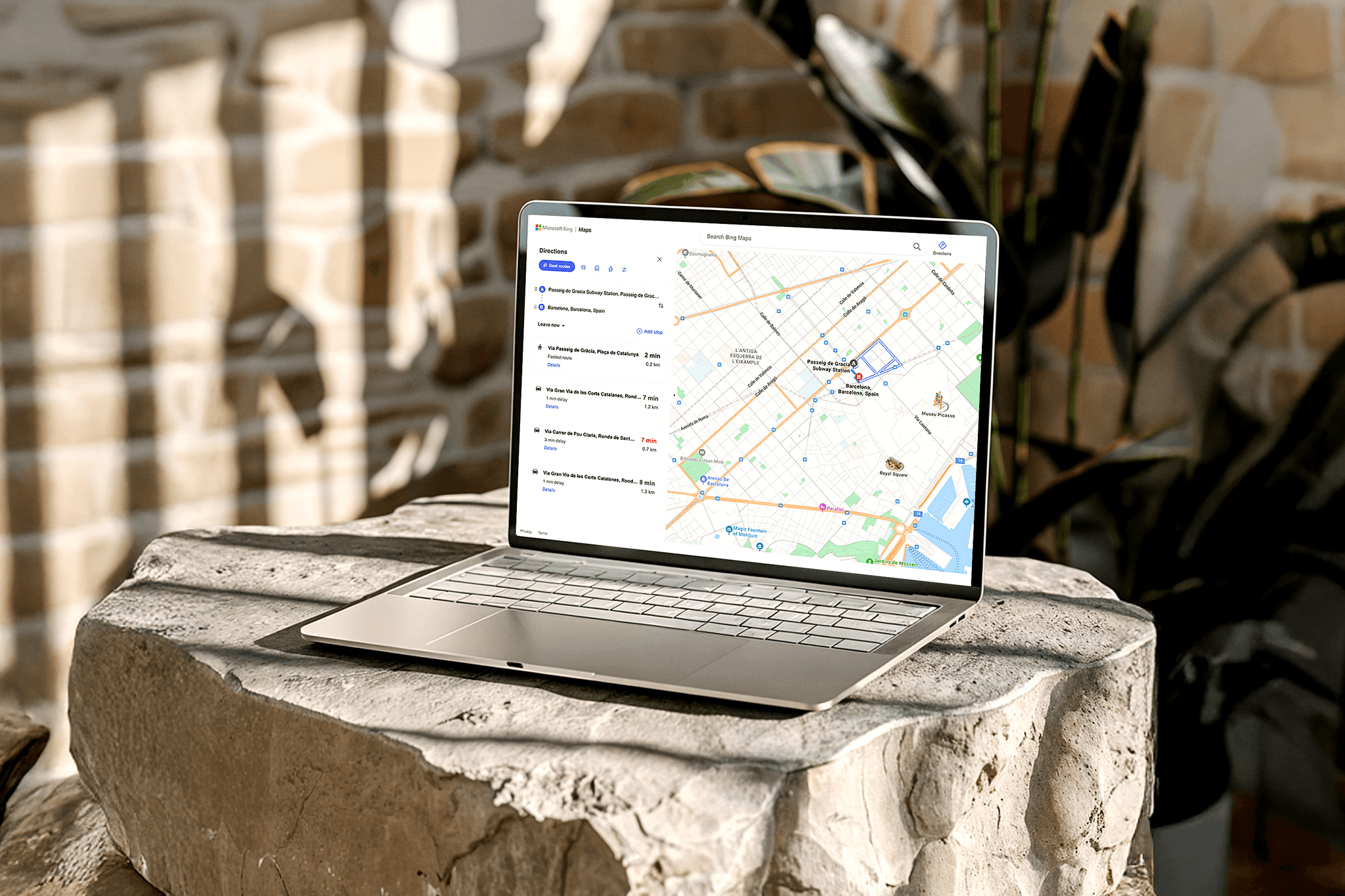 Laptop displaying the redesigned Microsoft Maps interface placed on a textured stone surface with warm natural light