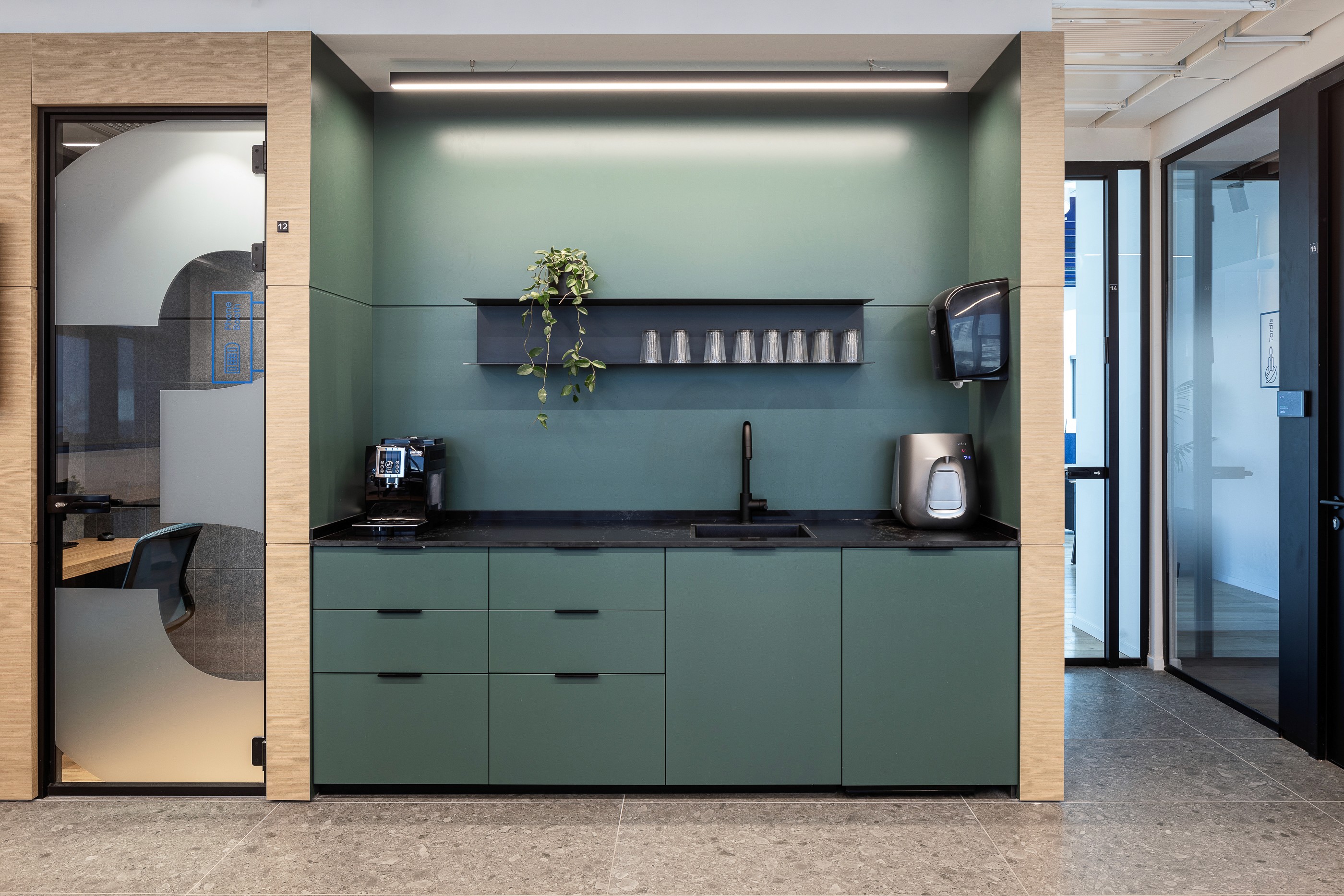 מטבחון משני (Coffee Point): נישת נגרות מעוצבת בגוון ירוק מרווה עם מסגרת עץ, המשמשת נקודת התרעננות נגישה במעבר.