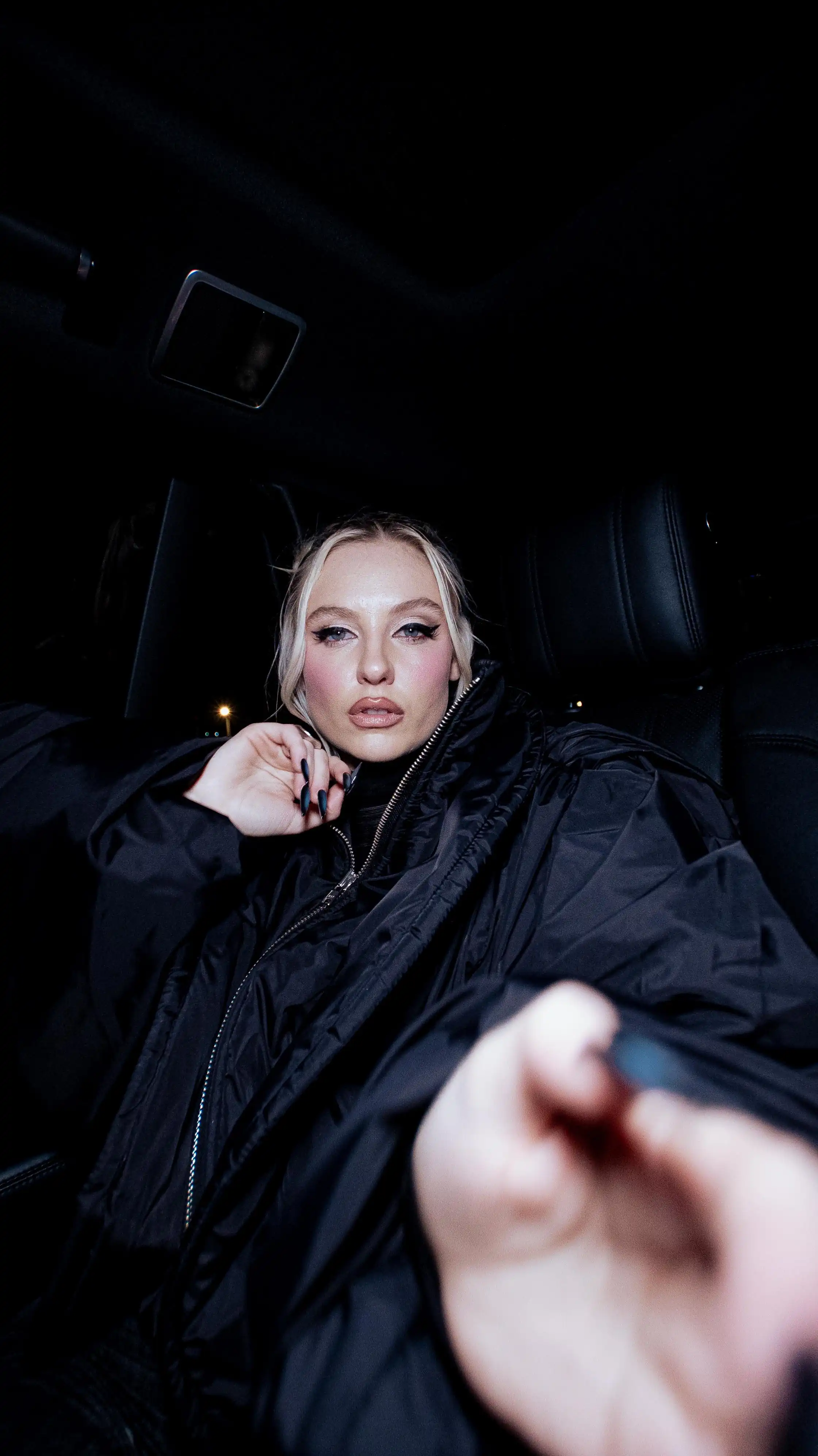 A girl dressed in black inside a car staring at a camera