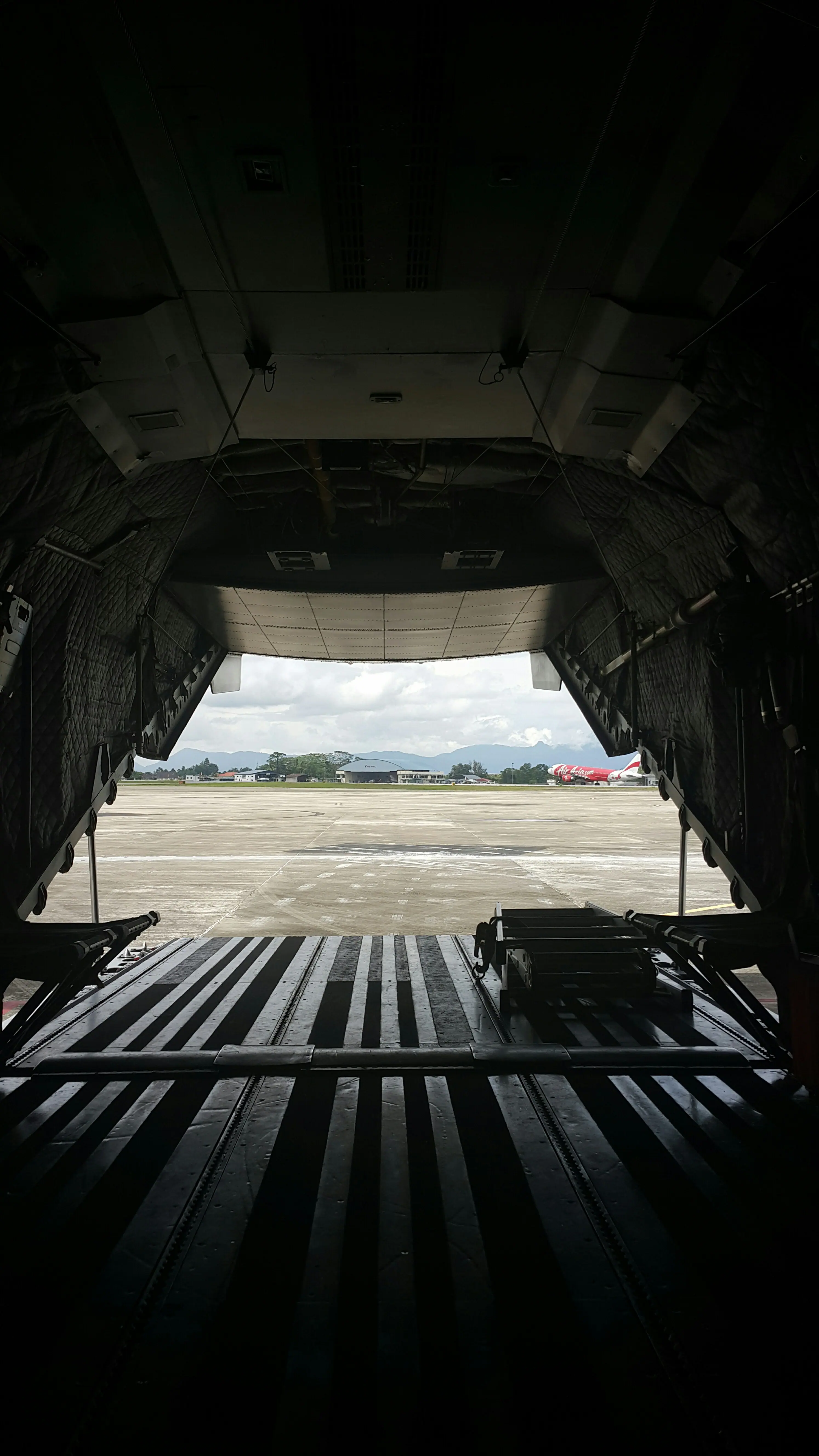 View from the interior of a military cargo plane looking out onto an airstrip, with mountains and buildings visible in the distance.