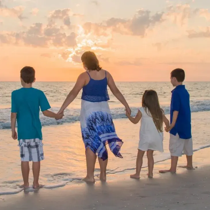 A family stands hand in hand on the sandy beach of Bradenton, FL, watching a vibrant sunset over the ocean.