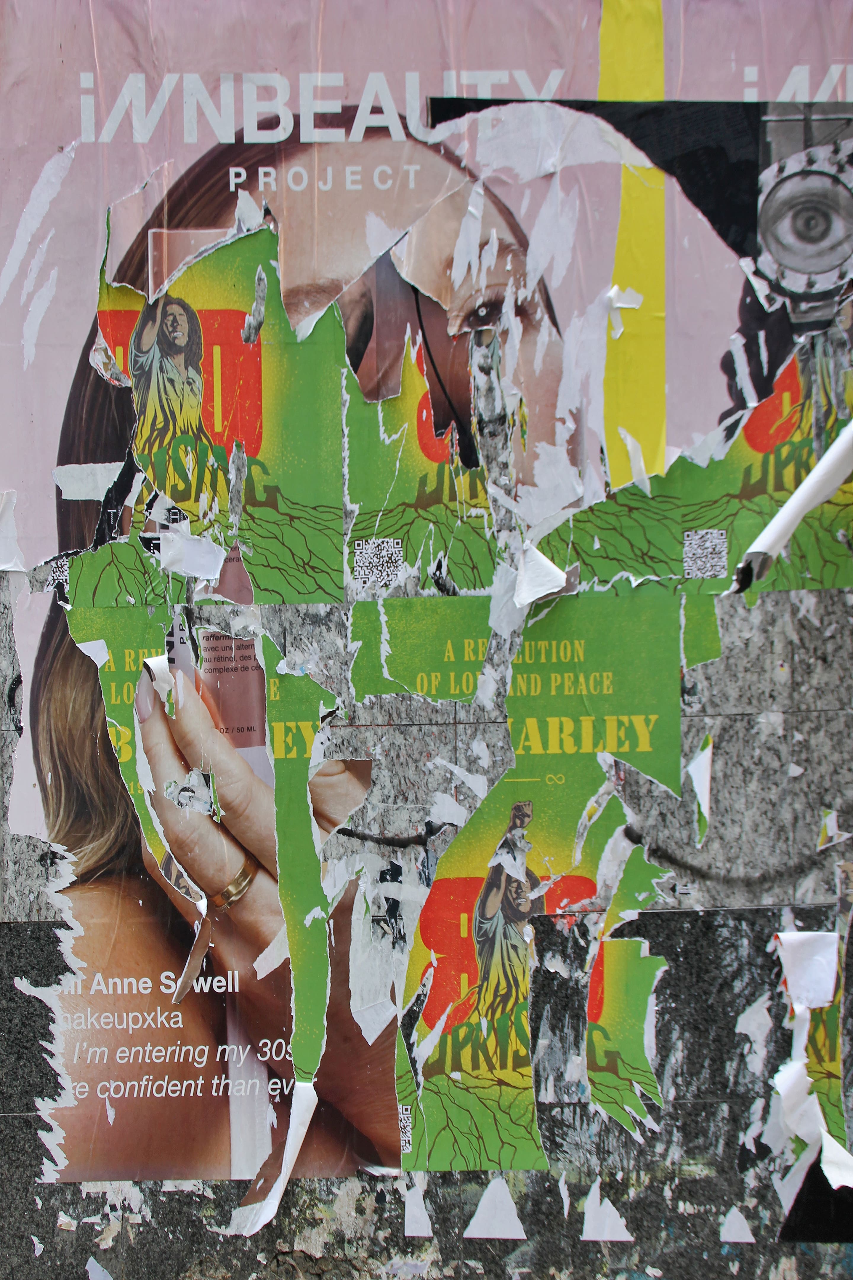Close-up photograph of overlapping torn posters combining fragments of a beauty ad and a green promotional print. The layered textures and exposed paper create an abstract visual field where consumer imagery dissolves into decay.