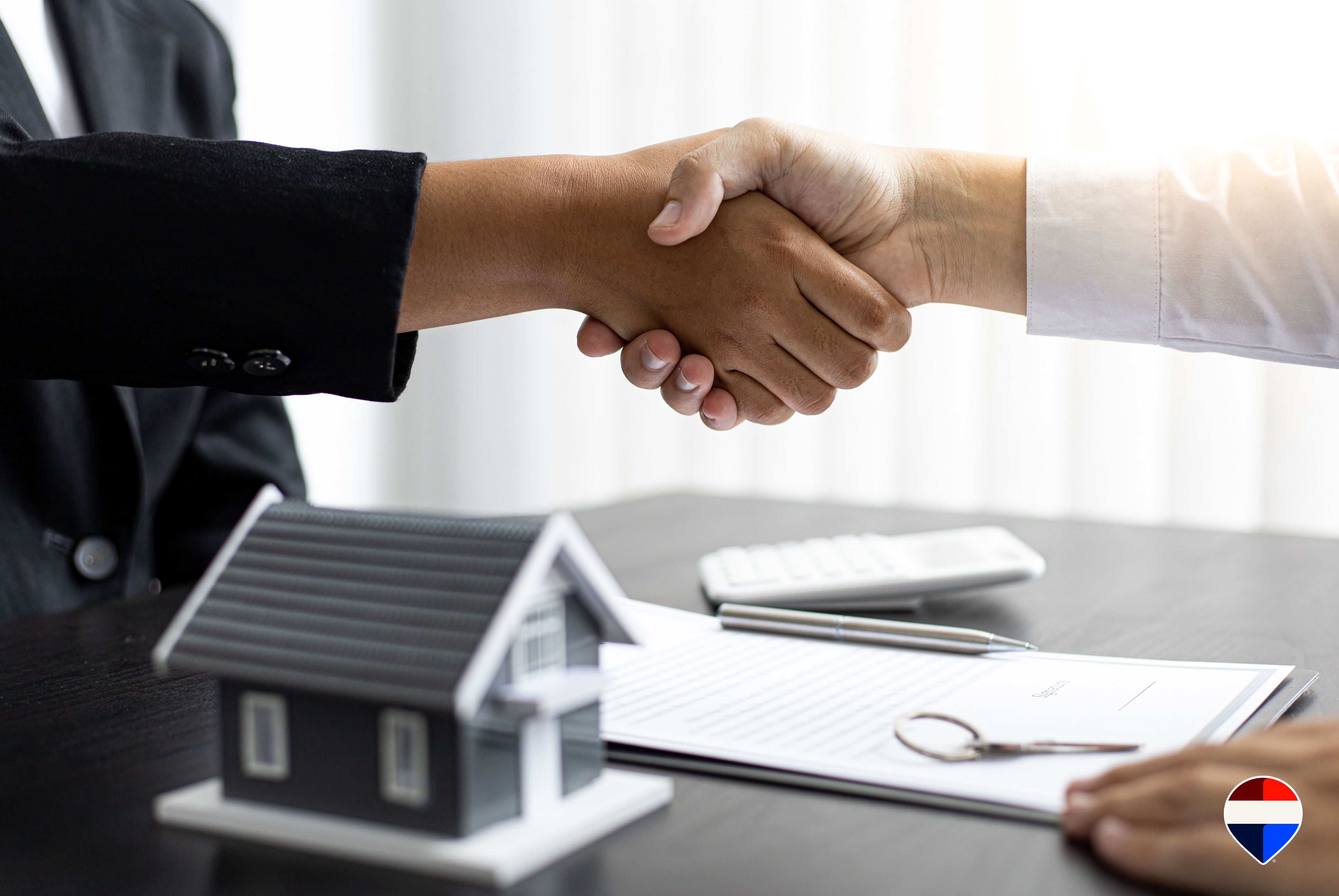 Stretta di mano tra agente immobiliare e cliente accanto a un modellino di casa e al contratto di vendita firmato
