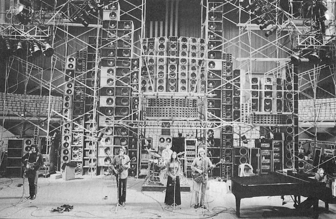 Black-and-white concert stage filled with speakers, scaffolding, musicians, and a grand piano.