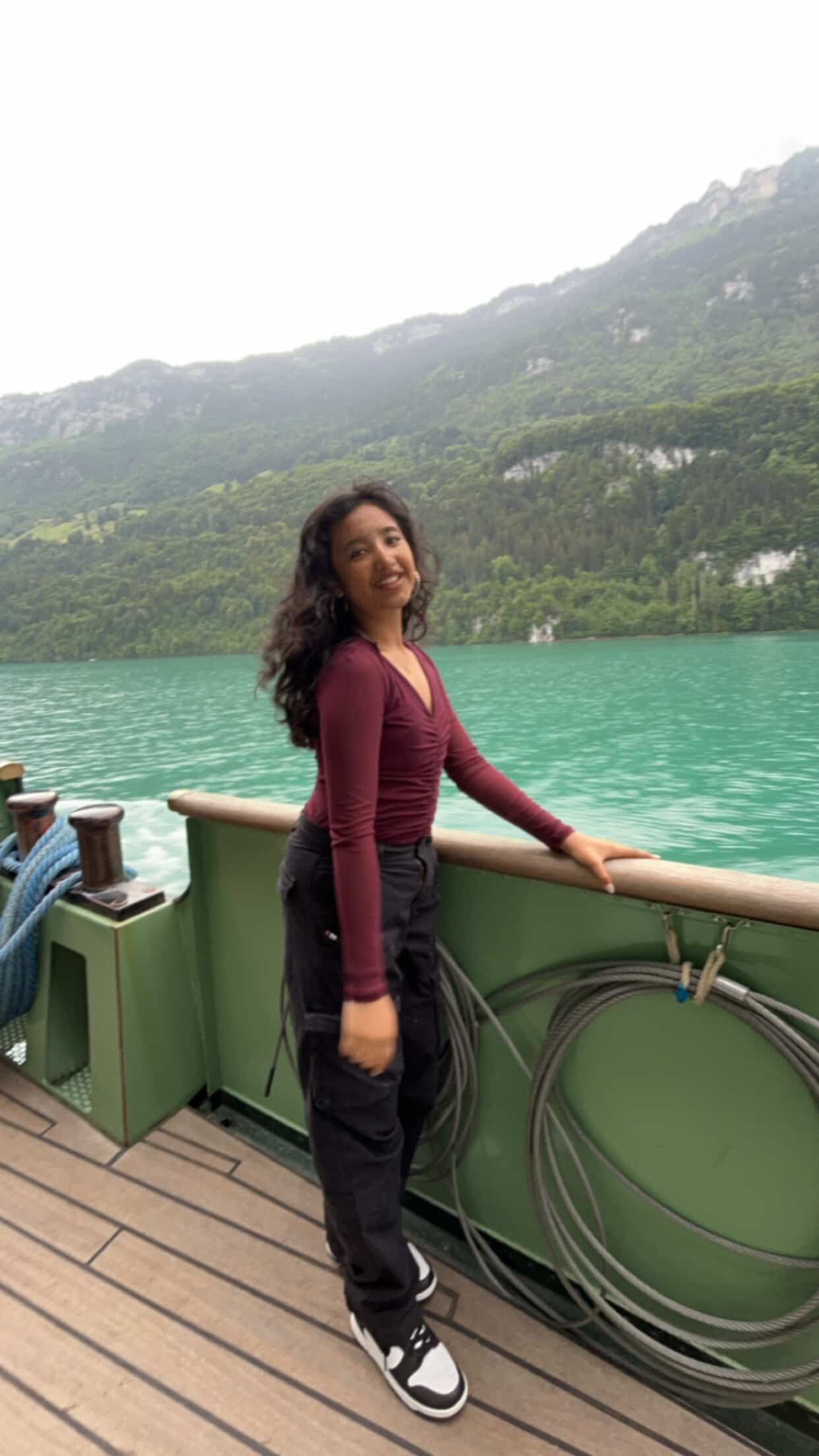 A smiling person with curly hair, wearing a leather jacket, stands in a cozy indoor setting.