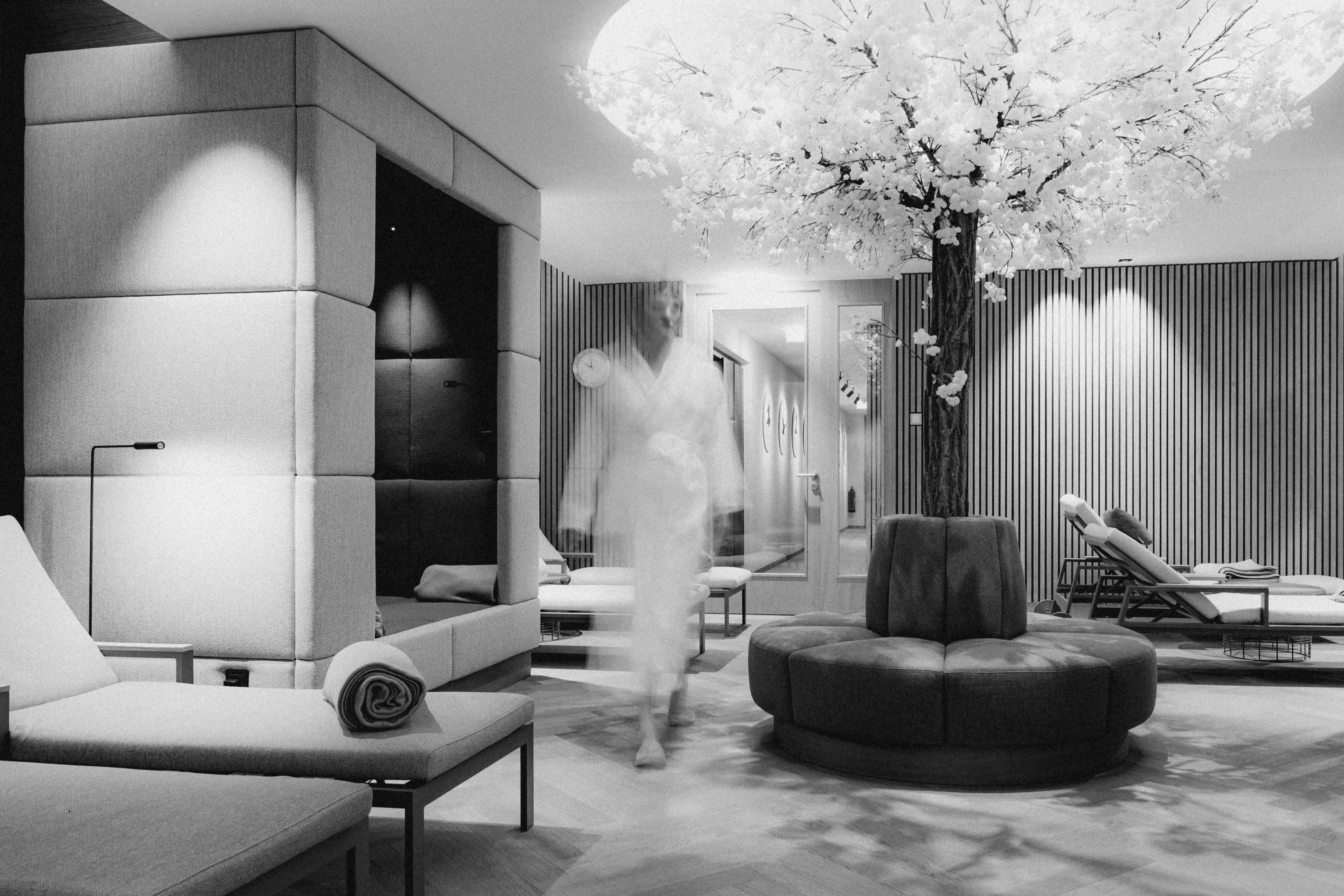 A modern lounge area with elegant furniture, soft lighting, and a decorative tree centerpiece. Monochrome setting.