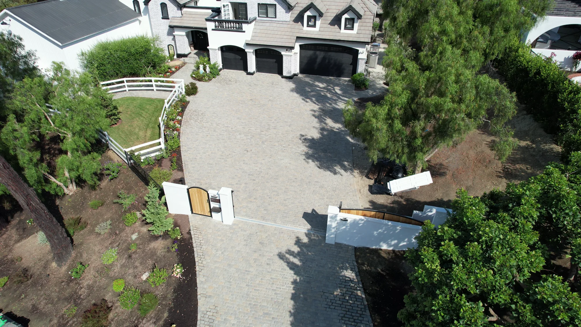 Elevated view of a gray paver driveway, open entrance gates and a white two-story home.