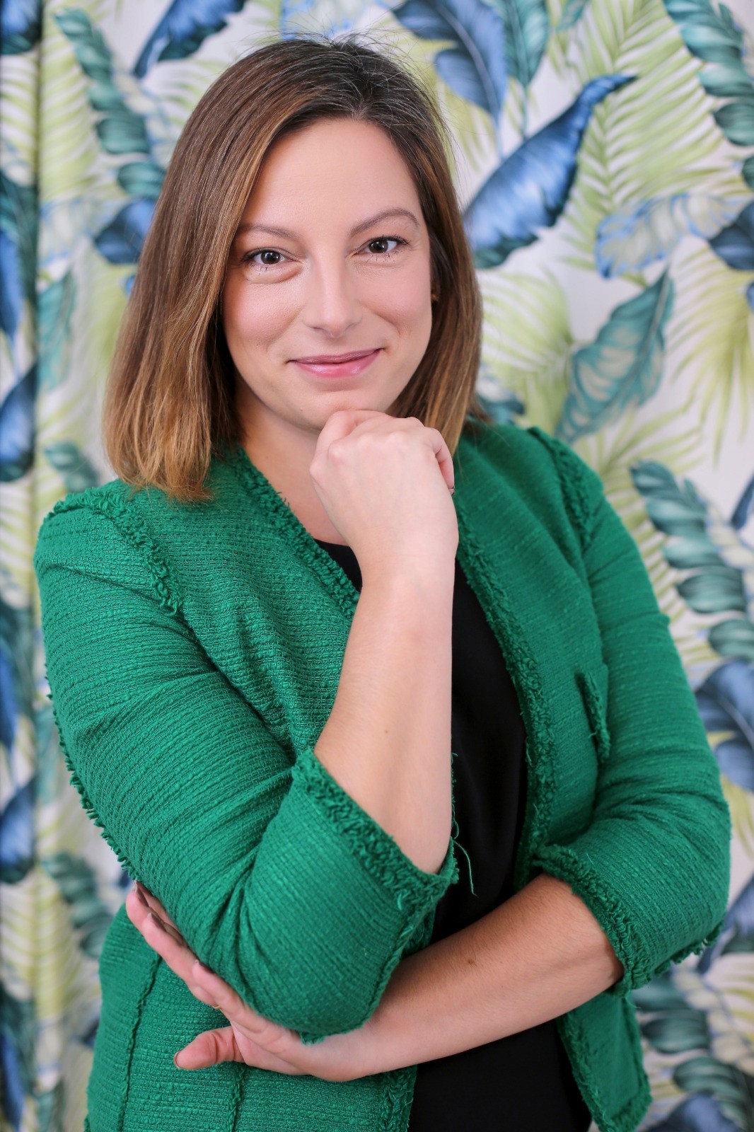 Smiling female therapist with short gray hair, wearing a brown top and a purple shawl, surrounded by a cozy background.