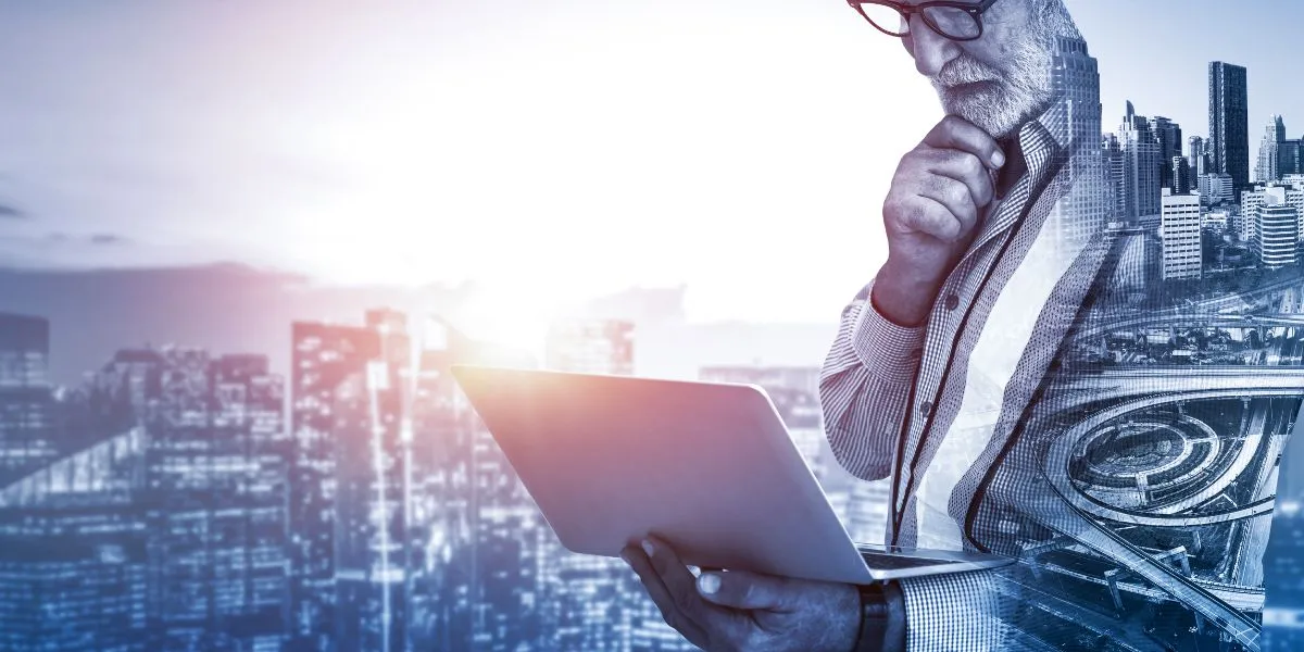 A man stands while two people sit at a table in an office setting, smiling and engaged in conversation. The mood is friendly and collaborative.