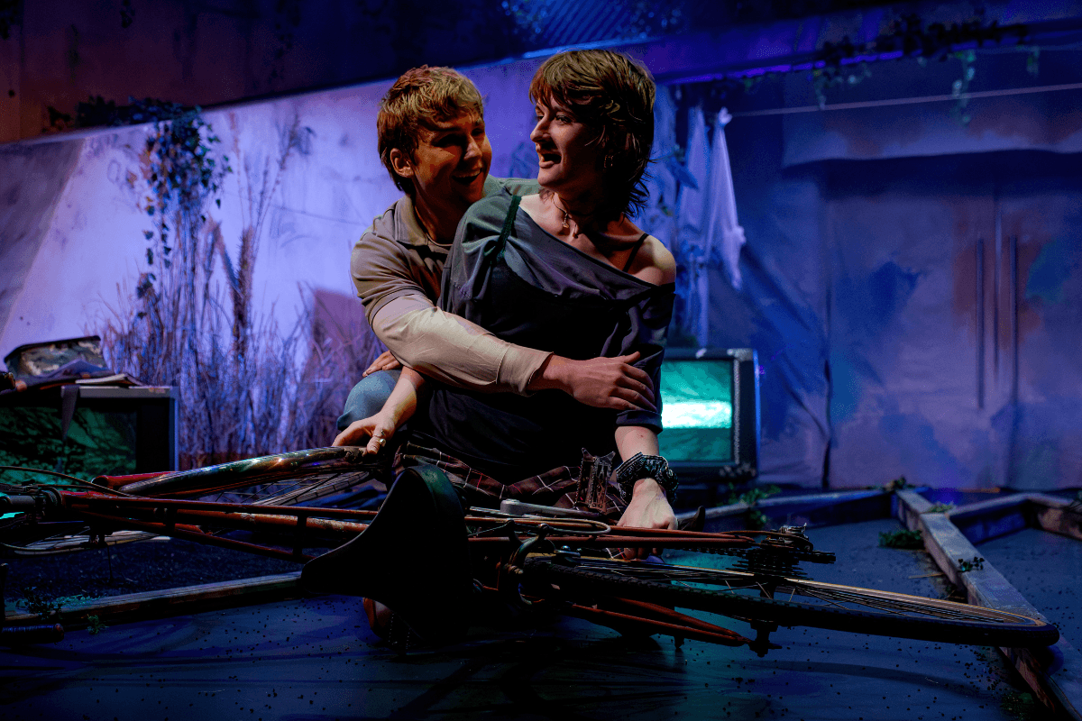 A boy embracing a girl from behind, who is holding a bike on the floor