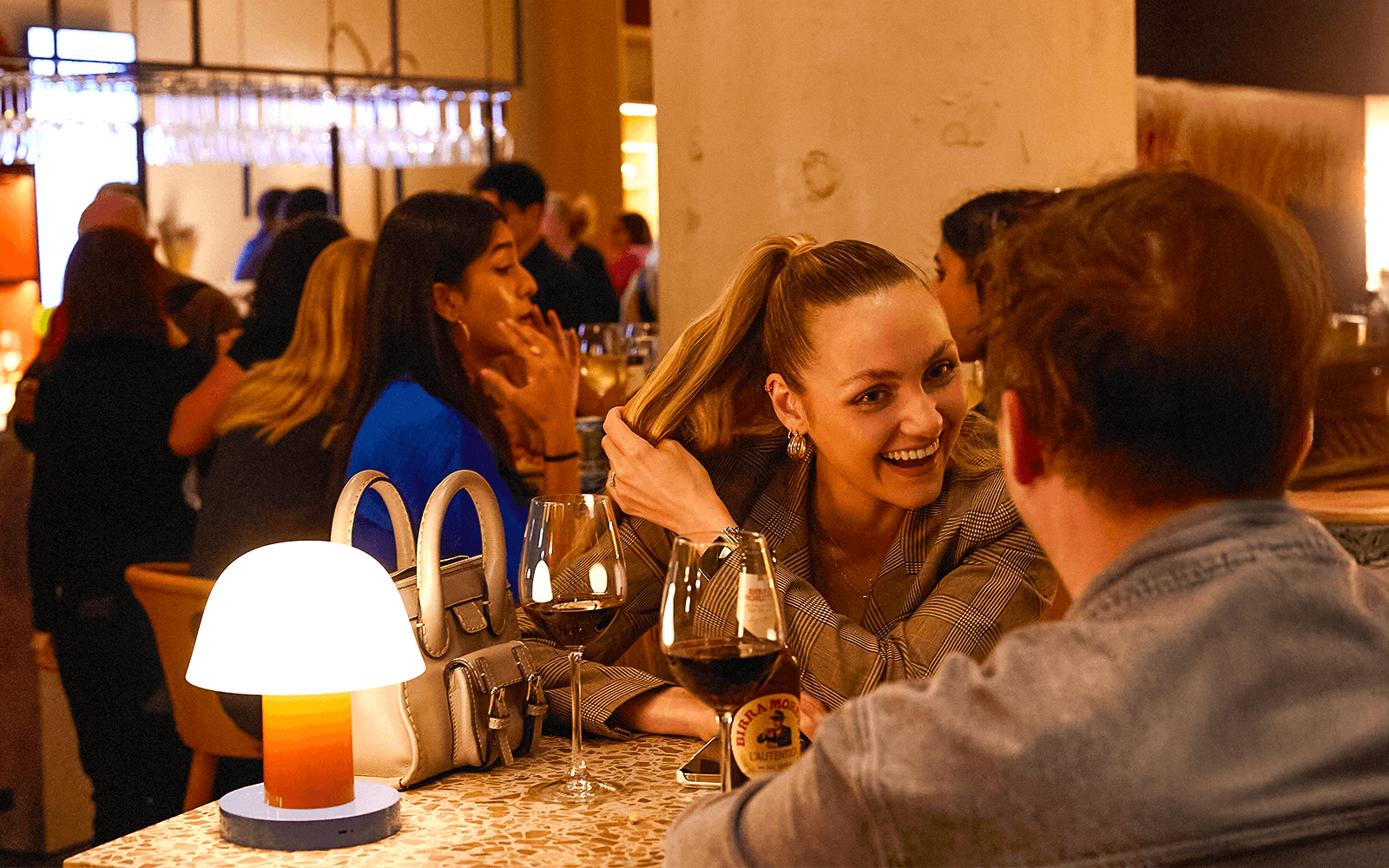 Orang ramai menikmati minuman dan perbualan di bar yang meriah.