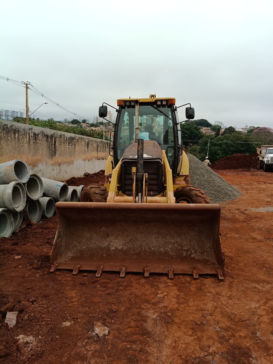 Retroescavadeira junto a tubos para execução de drenagem
