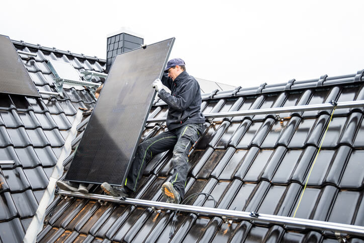 Eine Person klettert auf einem Dach und richtet ein großes Panel aus, vor dem Hintergrund weiterer Paneele.