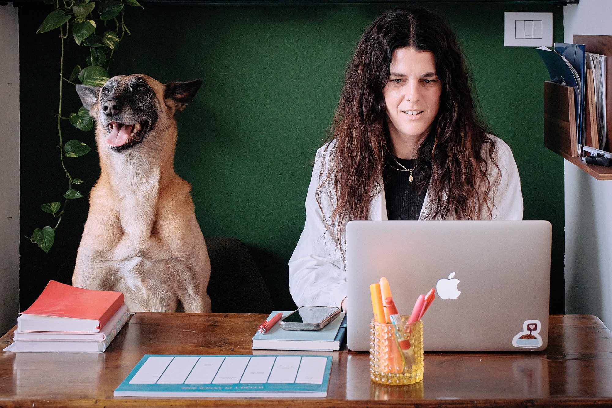 Veterinarian working at a desk with a smiling dog beside her, surrounded by books and stationery.