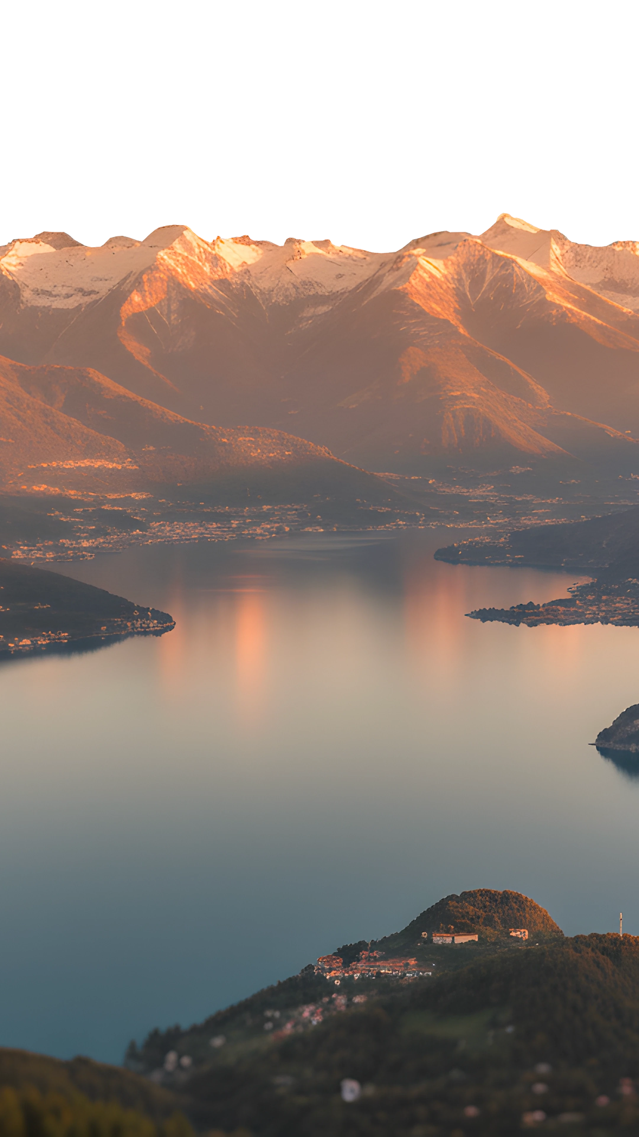 Vista panoramica del Lago di Como al tramonto, con riflessi dorati sulle montagne.