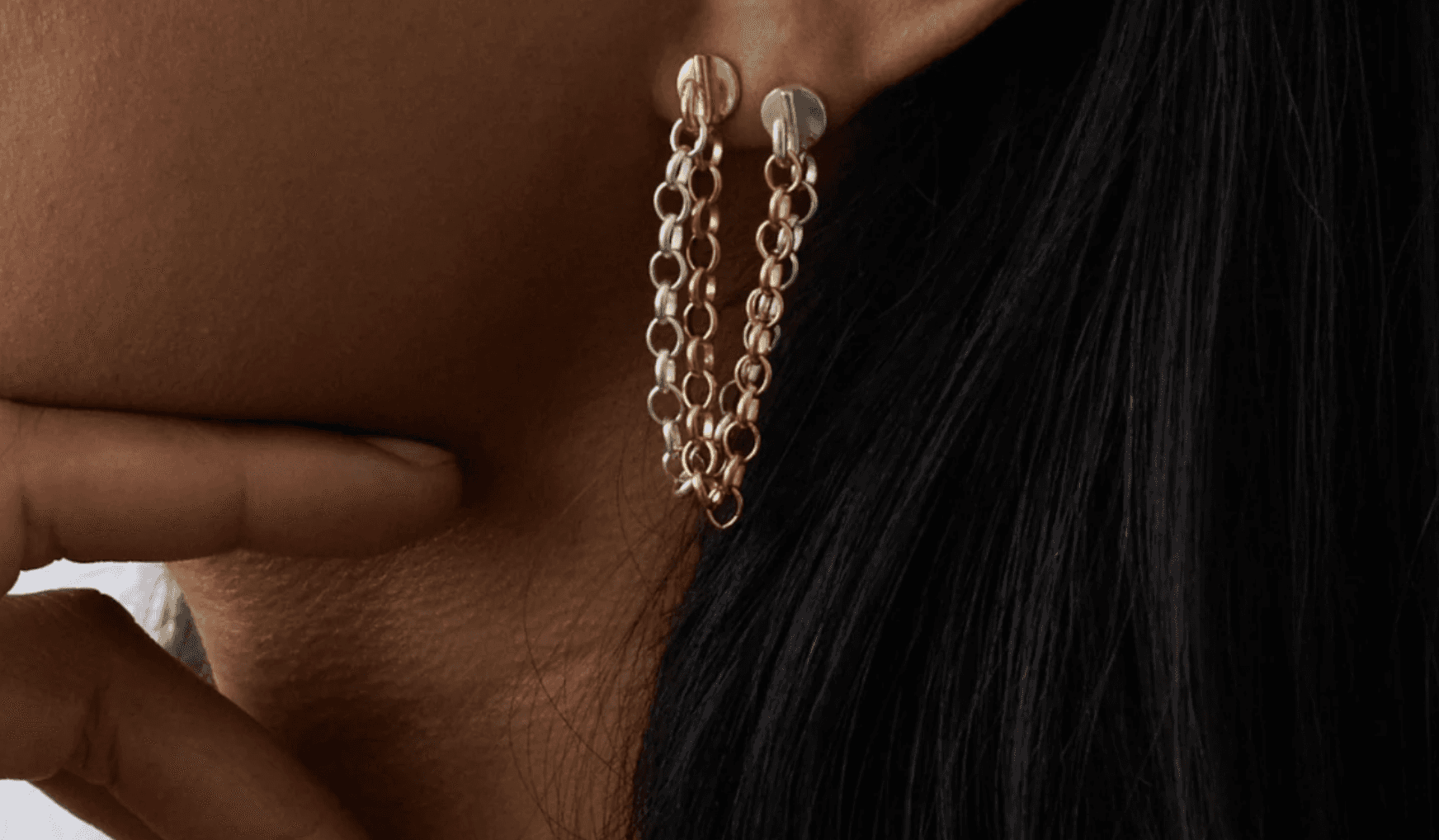 Two women standing closely together outdoors under a clear blue sky, looking directly at the camera, with blurred green leaves partially covering the foreground.