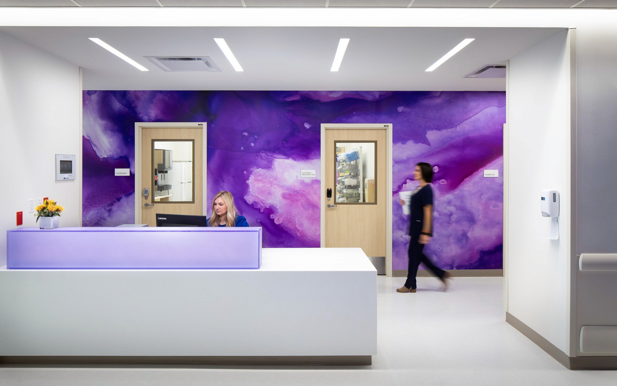 Reception desk with purple wall art and passing nurse.