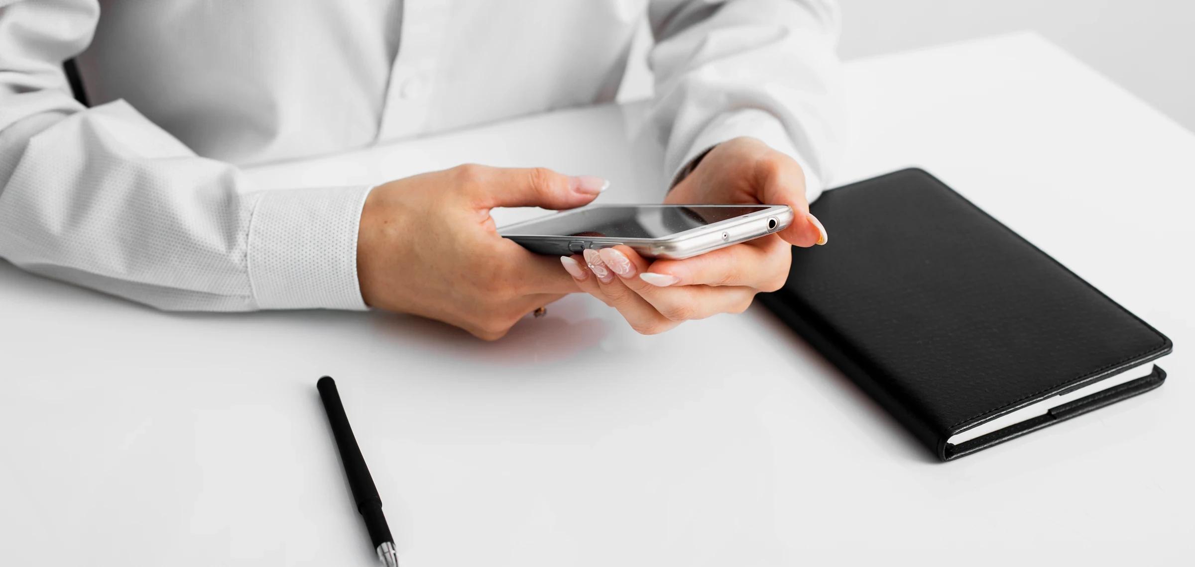 Человек в белой рубашке с телефоном за белым столом с блокнотом и ручкой