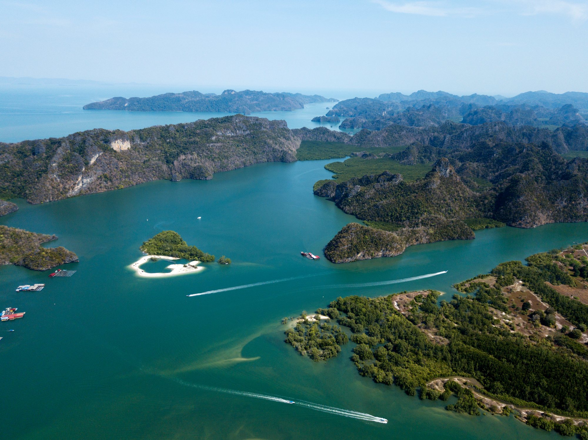 Boats running between limestone hills, mangroves and floating fish farms in the Kilim area, from above