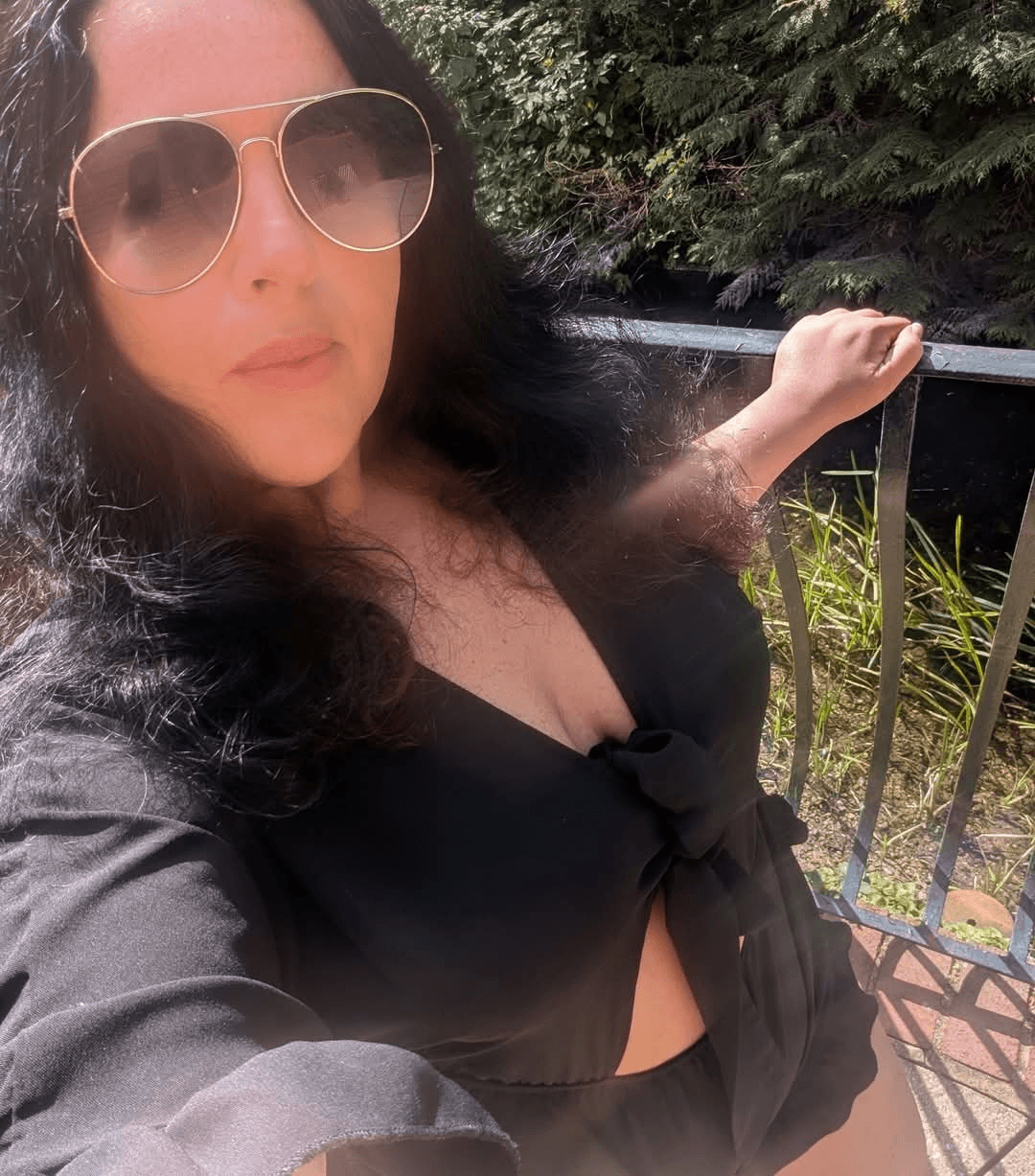 A stylish woman, Charlotte Alexandra, in sunglasses and a black top, exuding a chic and modern vibe.