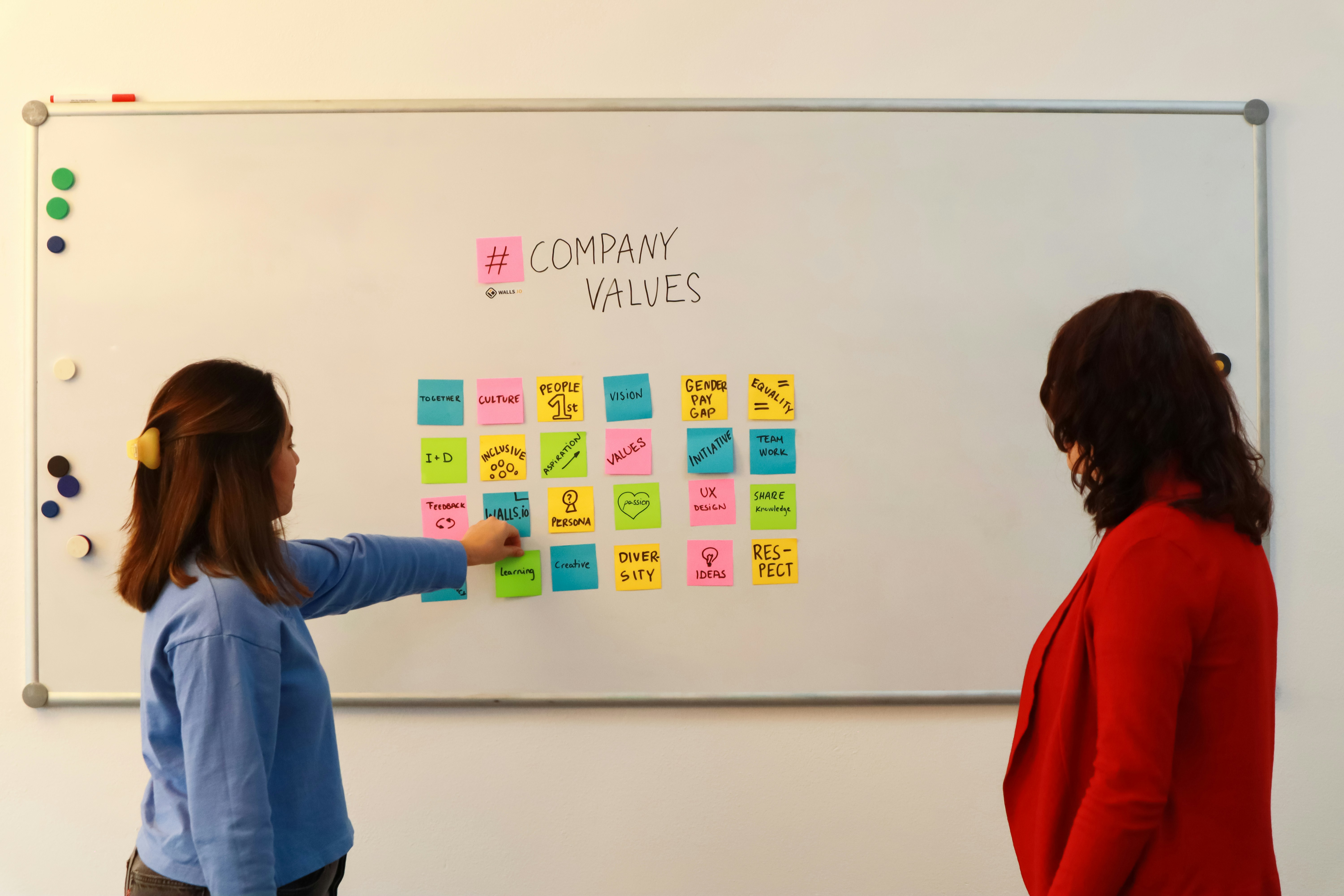 Two team members collaborating at a whiteboard covered in sticky notes during a hiring debrief