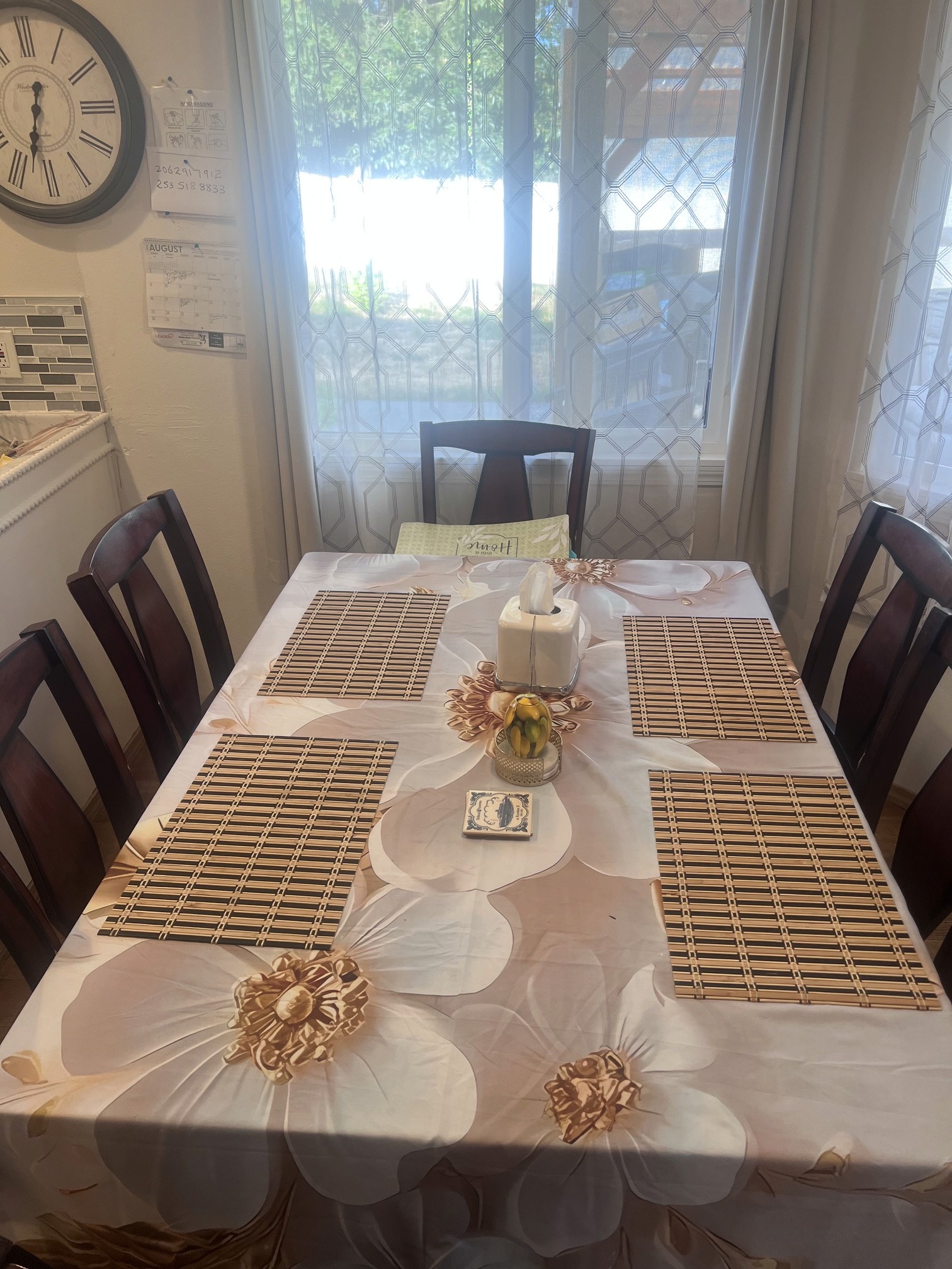 The dining table set with placemats for shared meals, beside a curtained window