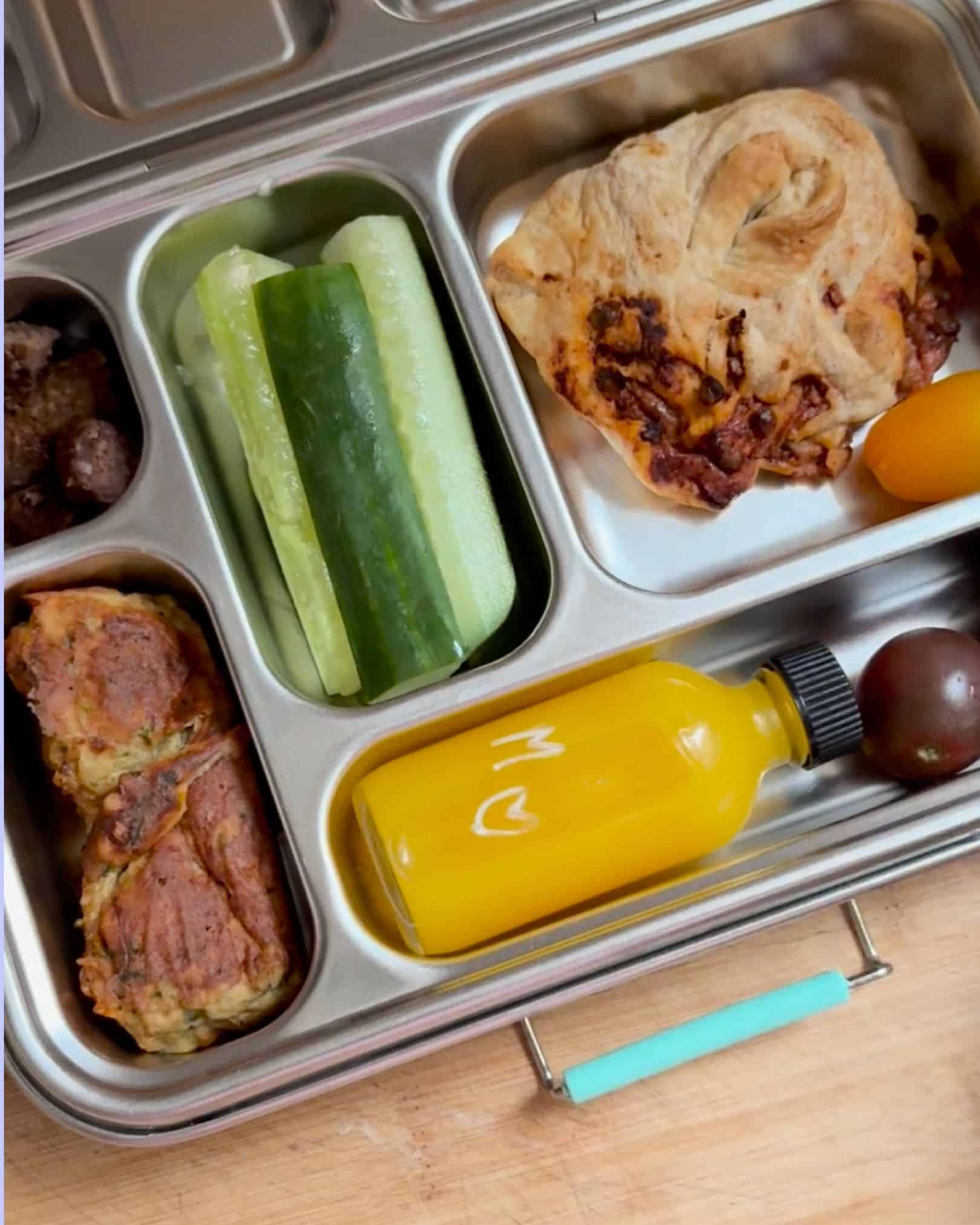 Example of a balanced Lunchbox Formula meal in a stainless steel bento box with vegetables, baked savory item, protein-rich fritters, fruit, and a reusable drink bottle.