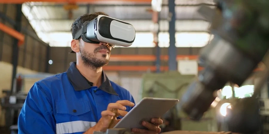 Engineer using a VR headset and tablet inside an industrial workshop to simulate or monitor machinery operations.