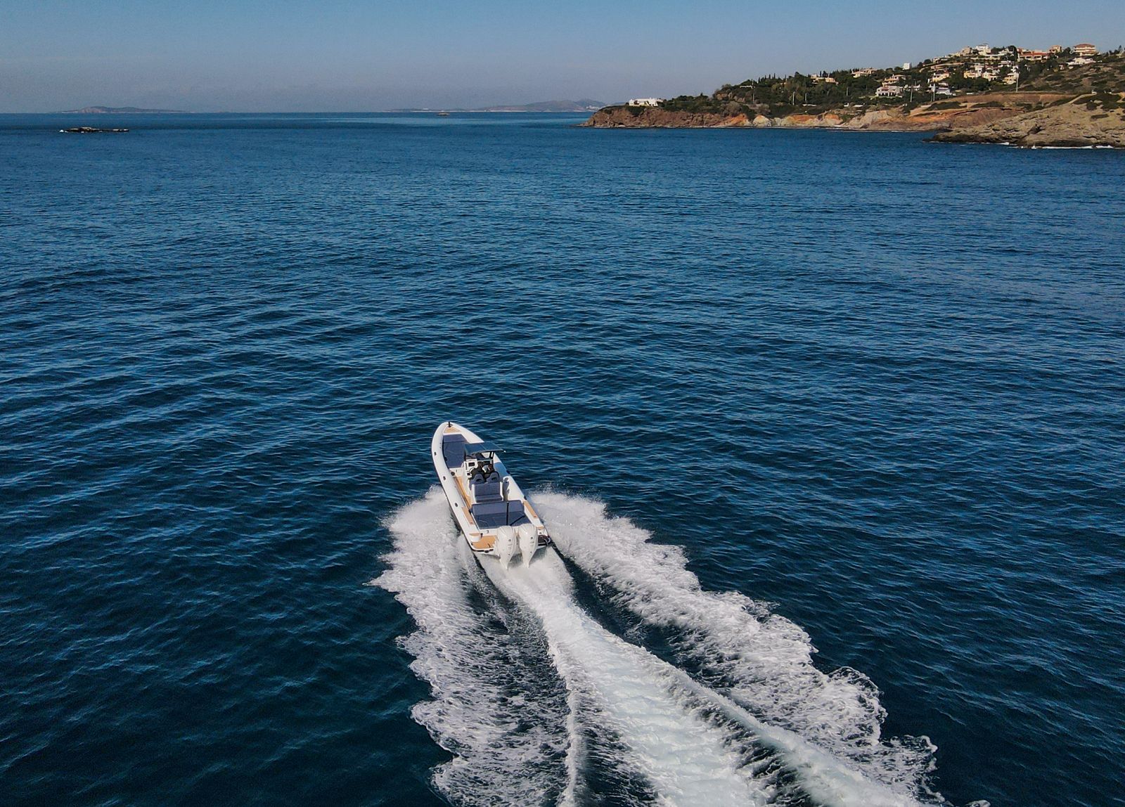 White Rock 36 speedboat with captain at helm cruising calm blue waters near Paros coastline with hills in background.