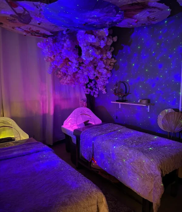 A smiling young man with crossed arms, wearing a plaid shirt and white t-shirt, poses against a dark background.