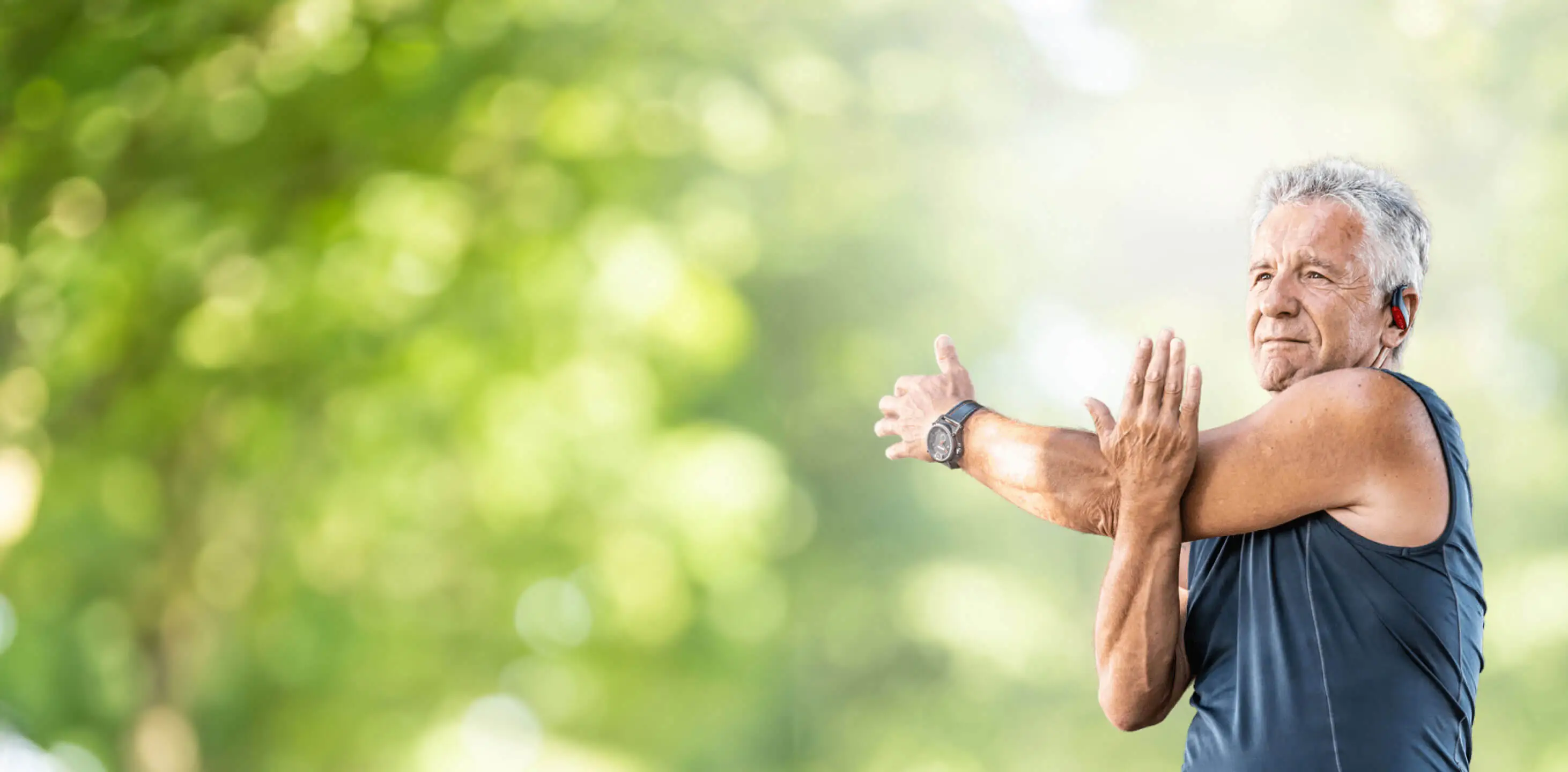 Elderly man stretching outdoors in a park, exercising for health and fitness.