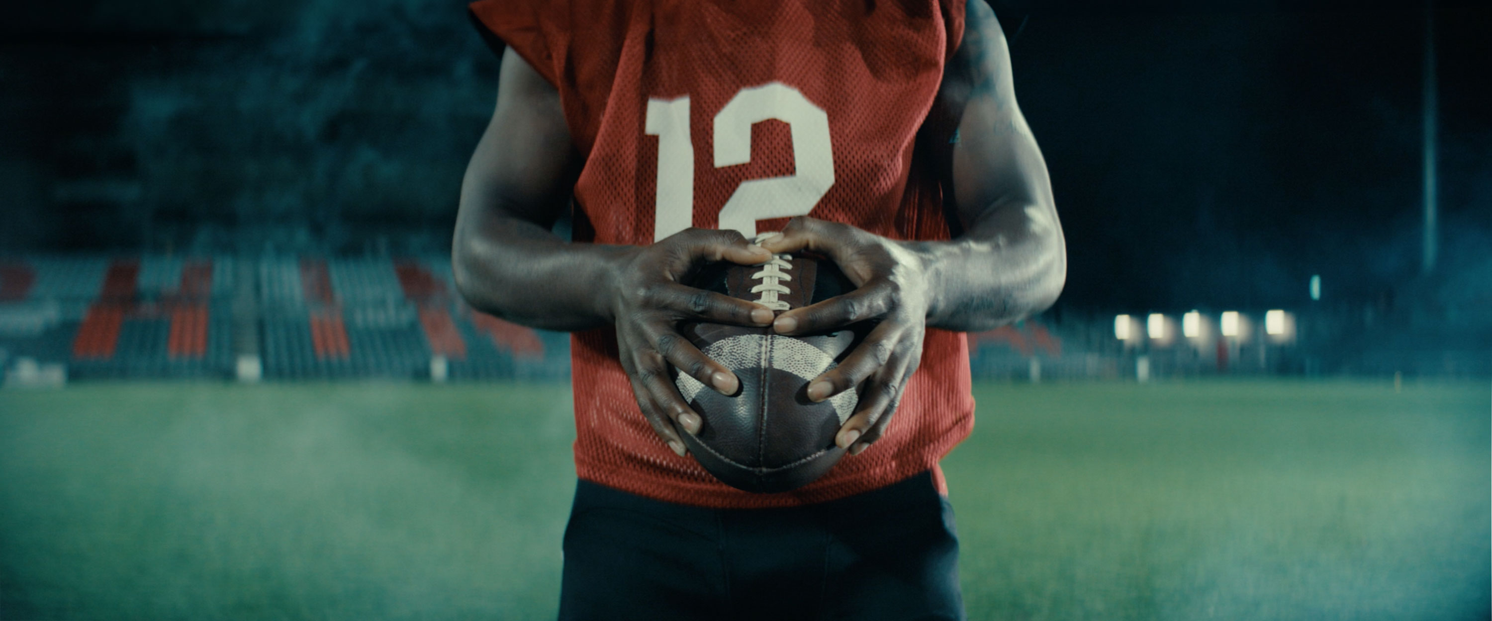 Football player in a red jersey holding a football on a dimly lit stadium field.