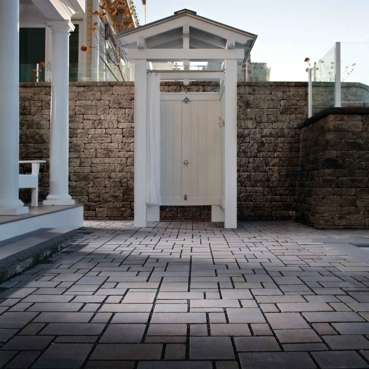 A finished side entrance Gray rectangular pavers leading to a white side gate between a house and garden wall.